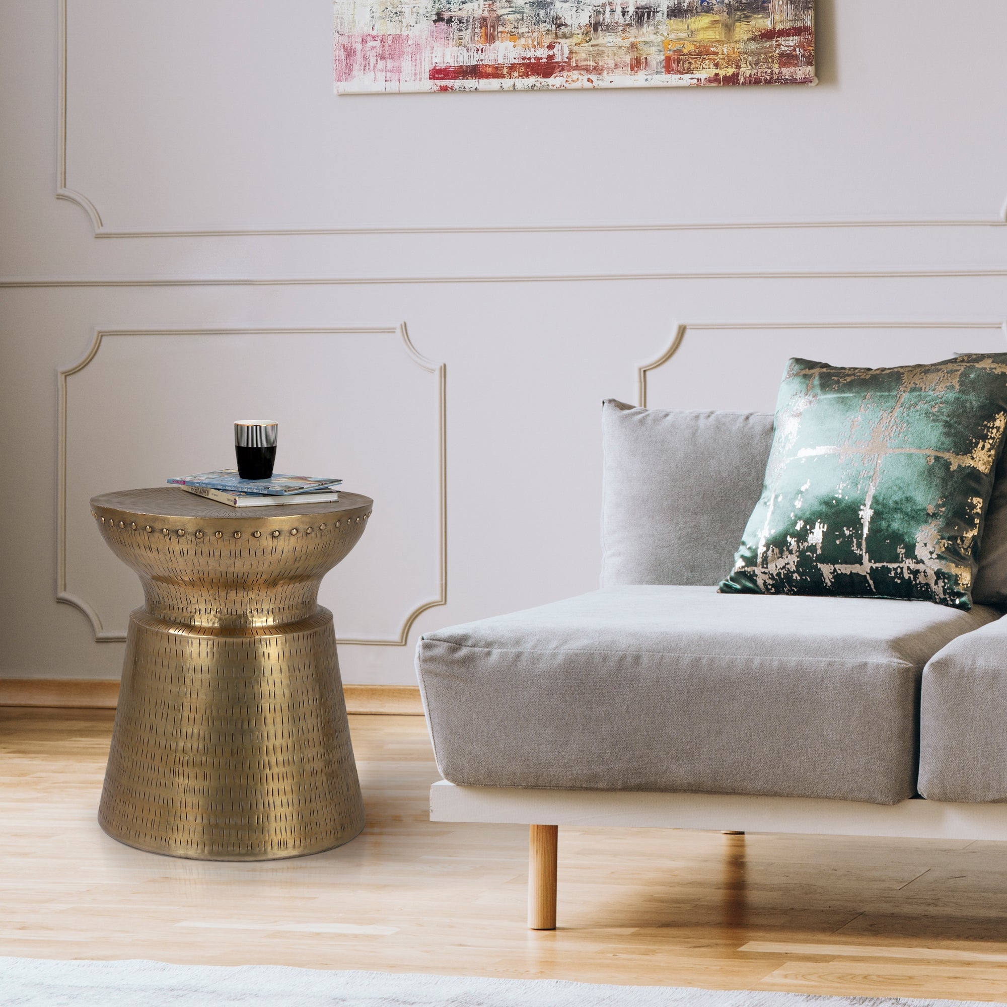 Soggiorno con tavolo dorato, divano grigio e cuscino decorativo.