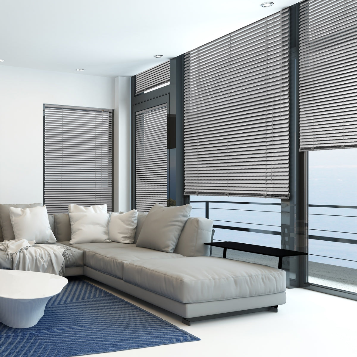 Wohnzimmer mit grauem Sofa und silbernen Jalousien an großen Fenstern.