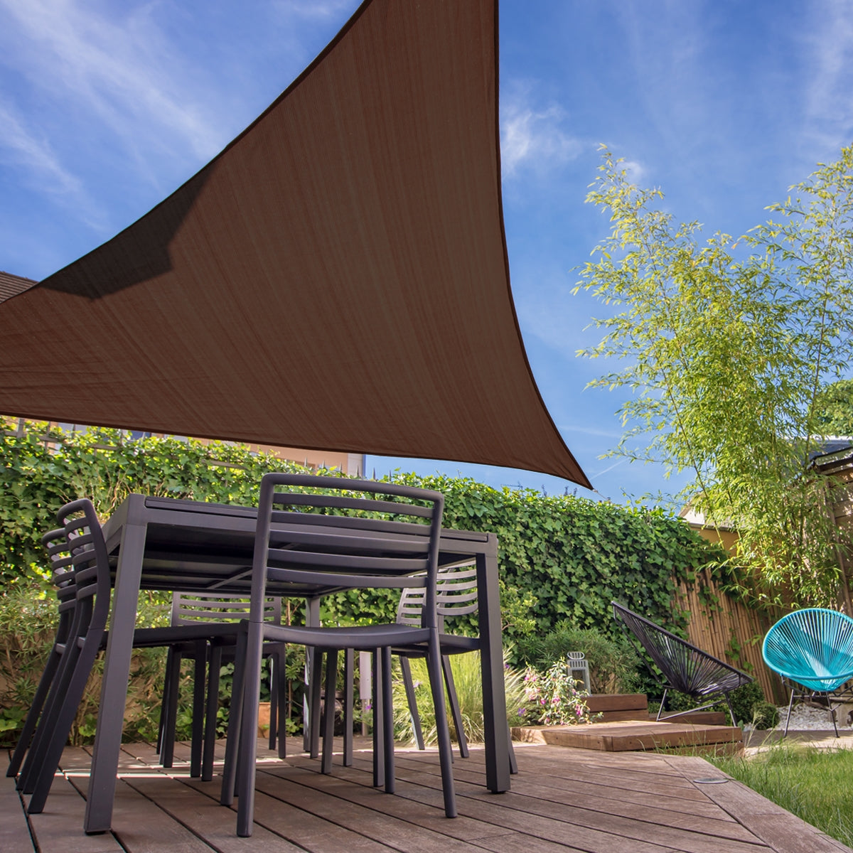 Garten mit einem braunen, dreieckigen Sonnensegel über einem Tisch und Stühlen.