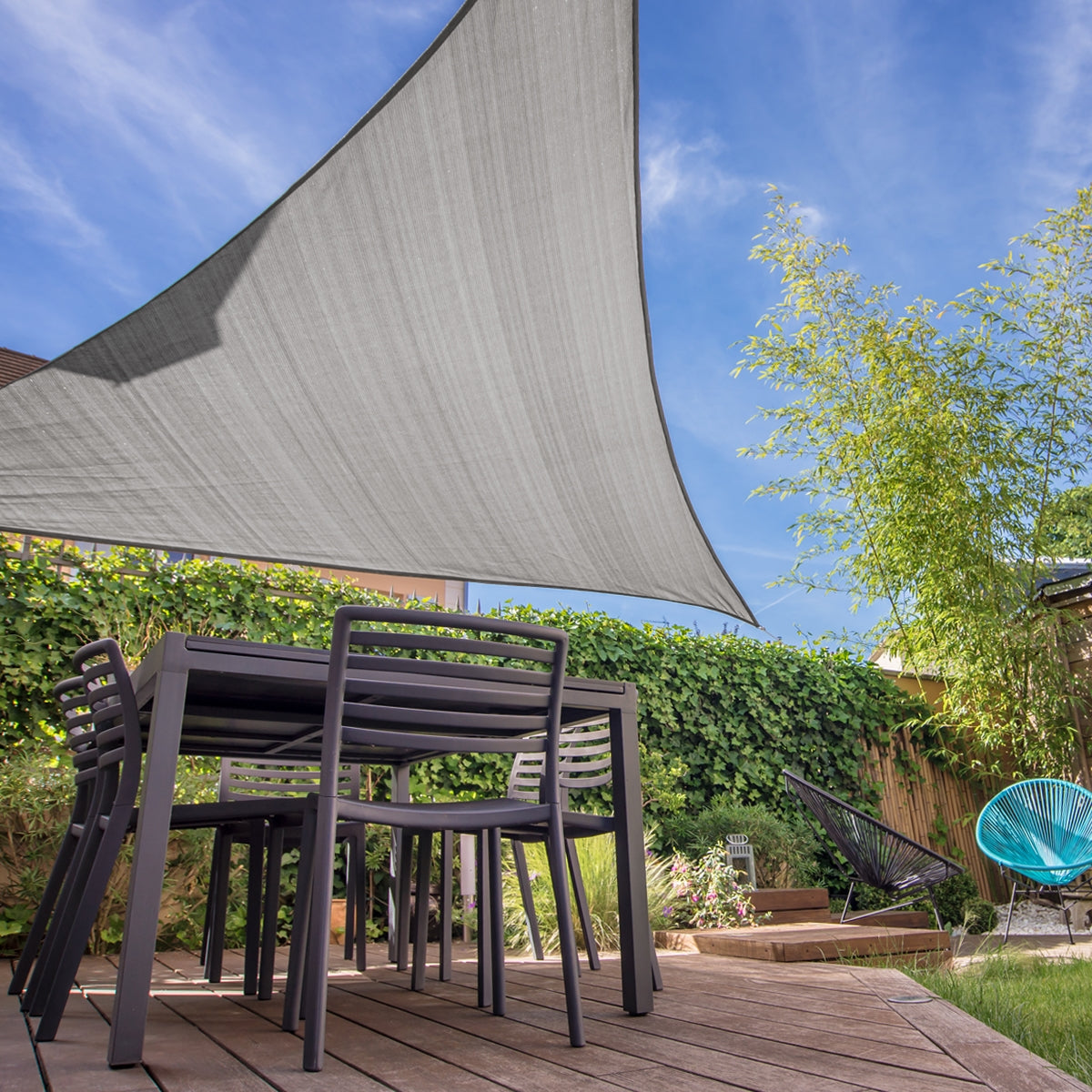 Jardín con un toldo triangular gris sobre una mesa y sillas.
