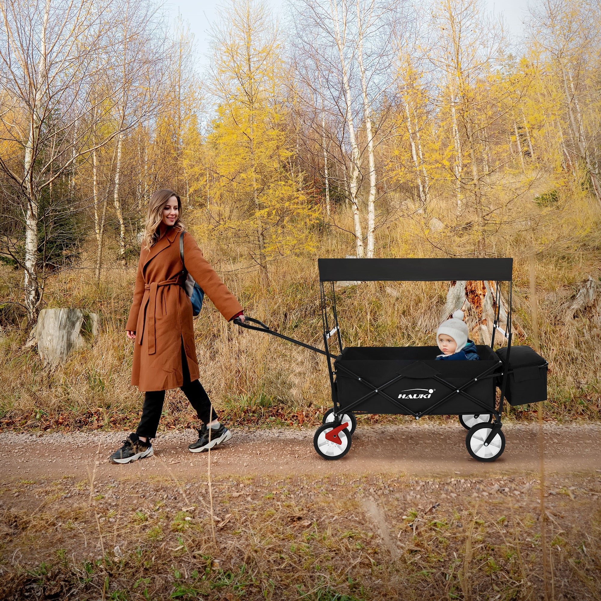 Frau zieht einen Kinderwagen auf einem Waldweg.