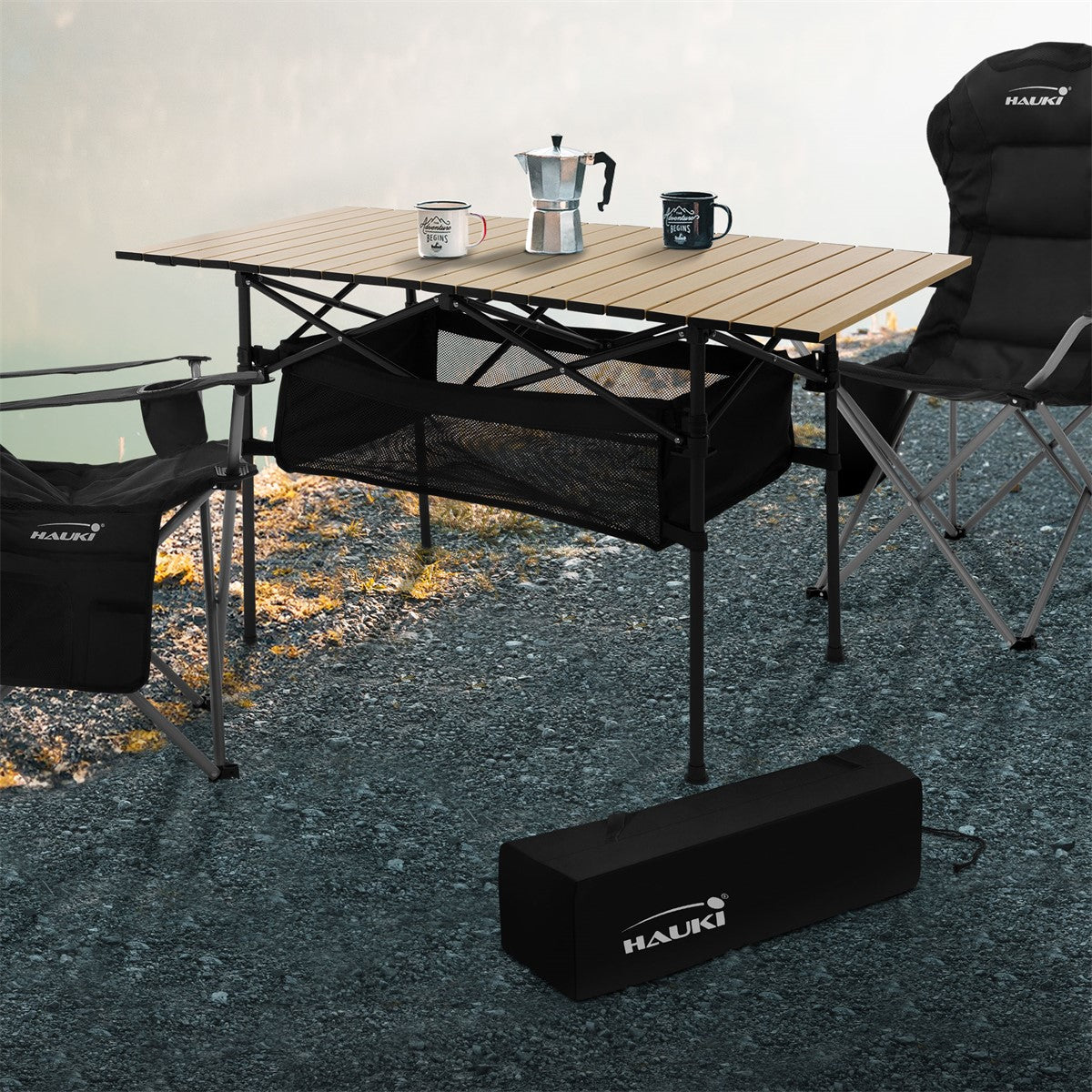 Camping table with two chairs, cups and a coffee pot outdoors.
