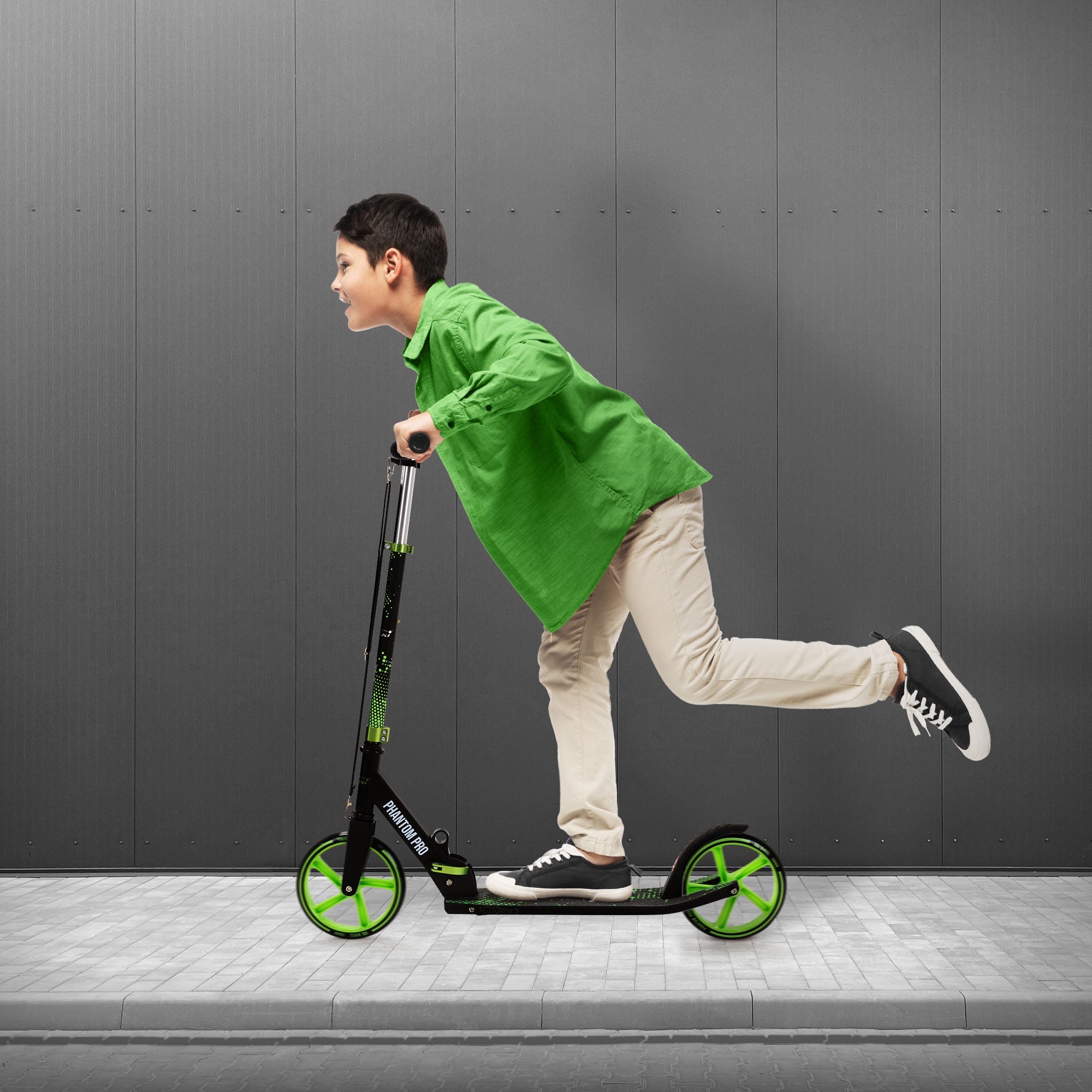 Ein Junge fährt auf einem grünen Roller auf einem Gehweg.