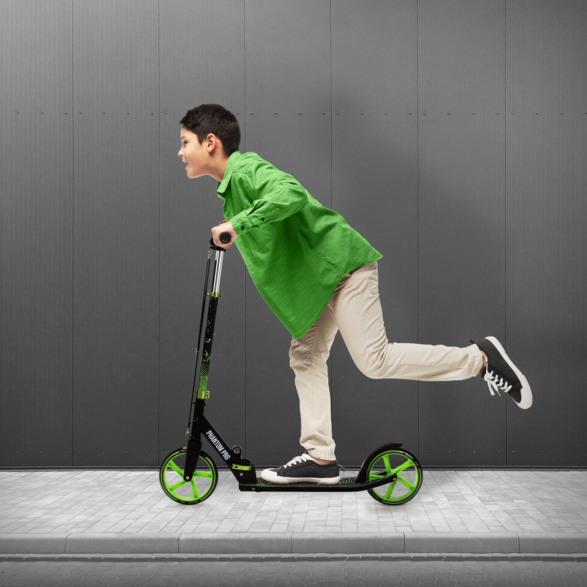 Ein Junge fährt auf einem grünen Roller auf einem Gehweg.