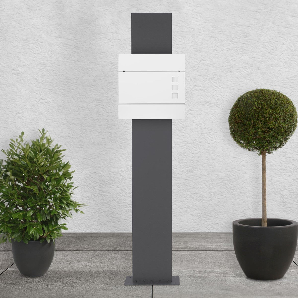White mailbox on a gray stand, surrounded by two plants.