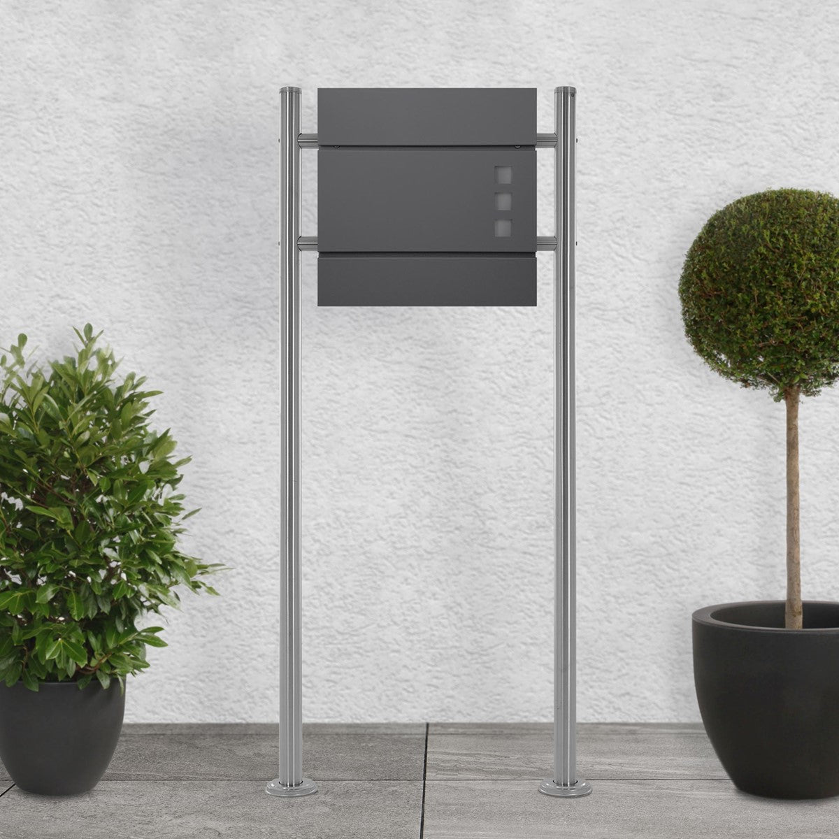 Black mailbox on two supports next to two round plants.