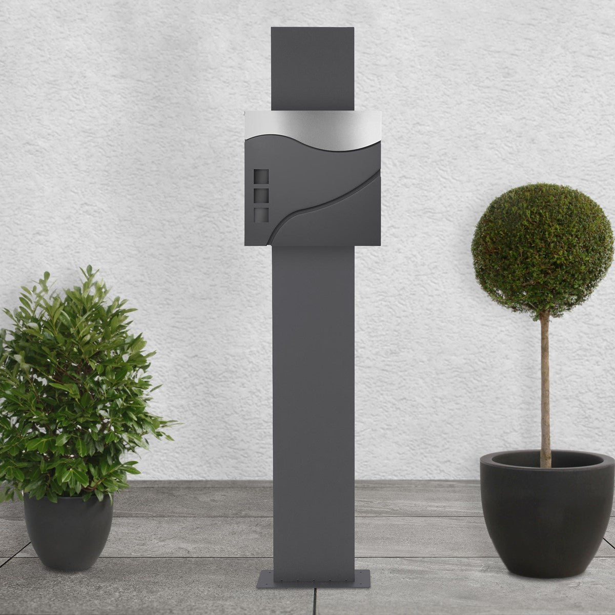 Anthracite mailbox with decorative plants in the background.