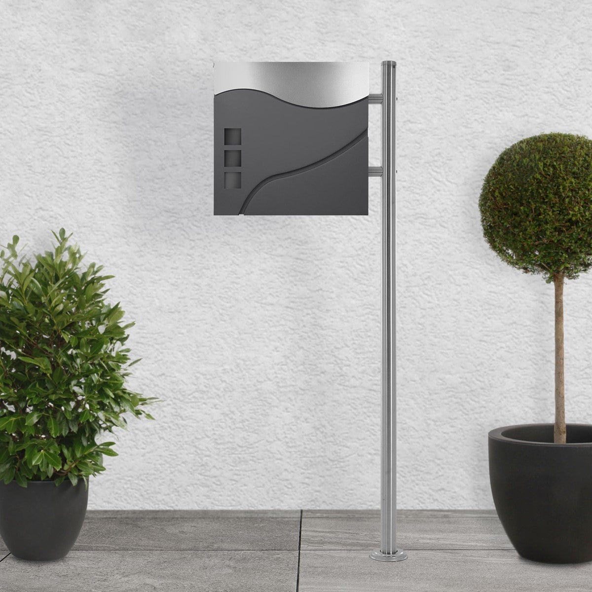 Modern mailbox on a stand, surrounded by plants.