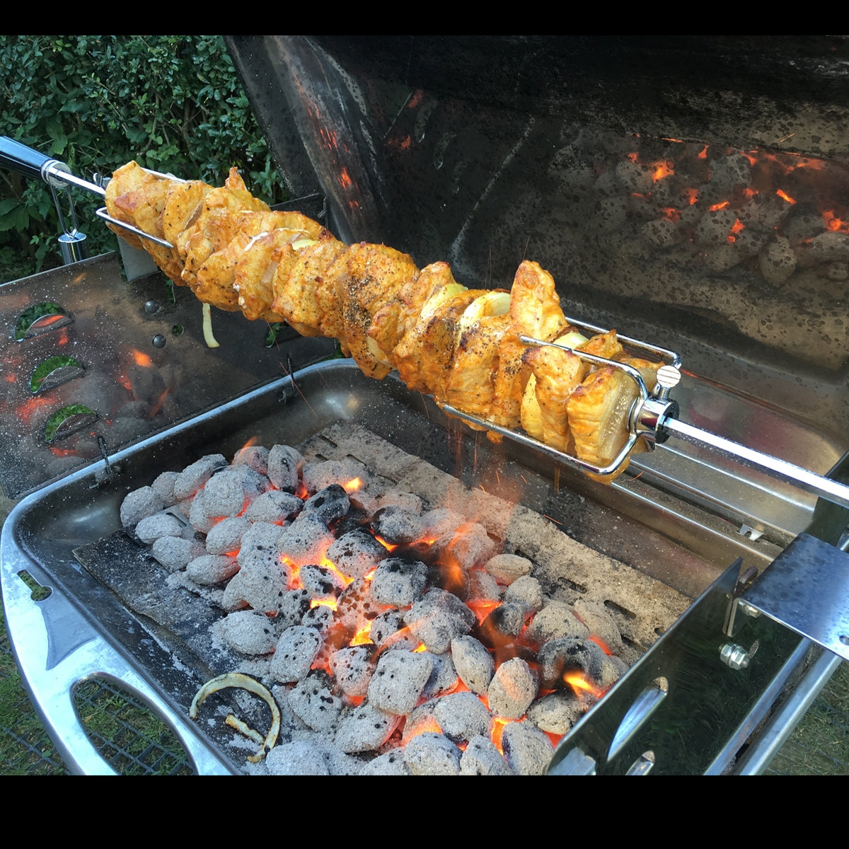 Hähnchen am Spieß über glühenden Kohlen auf einem Grill.