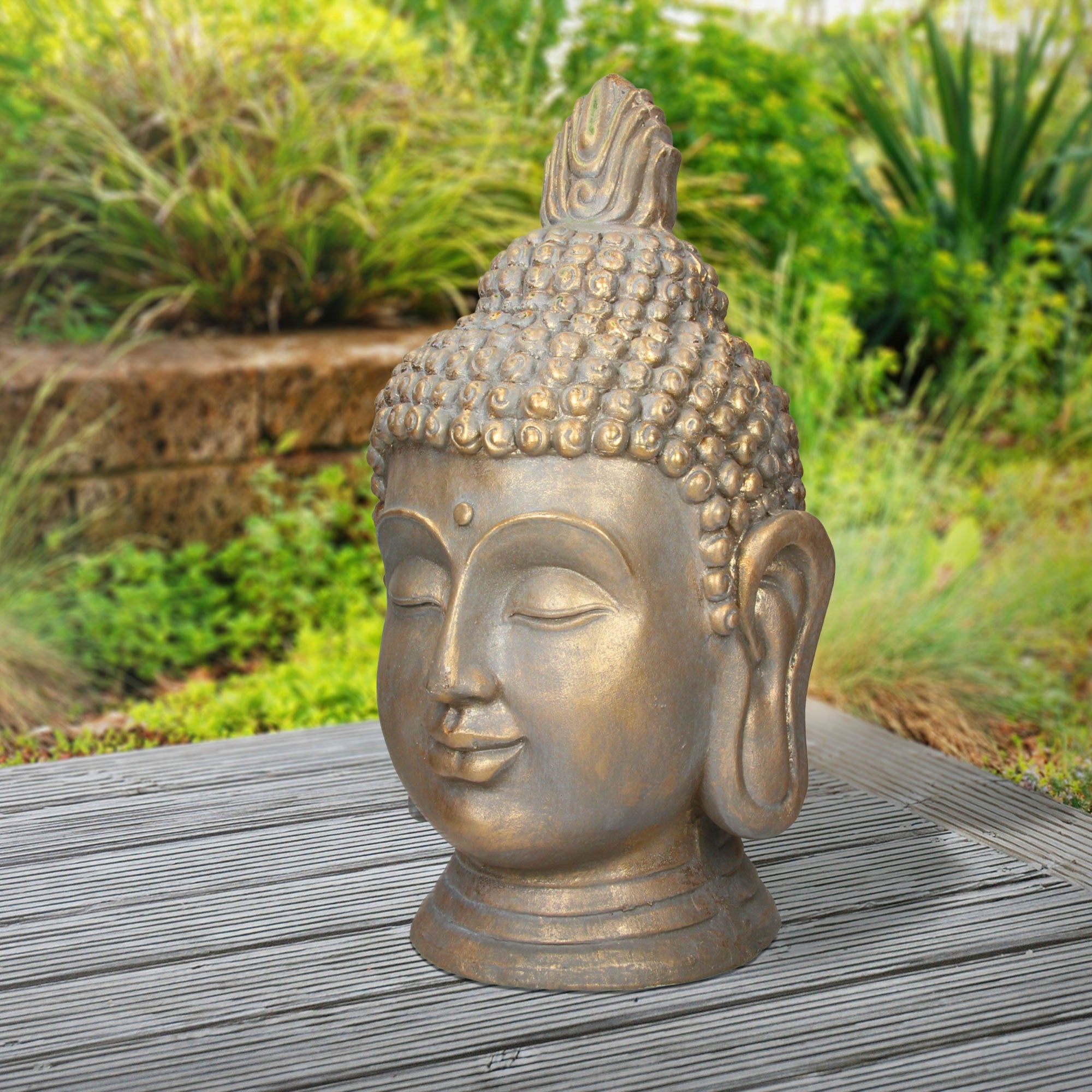 Buddha-Kopf aus Bronze auf einem Tisch im Freien, umgeben von Pflanzen.