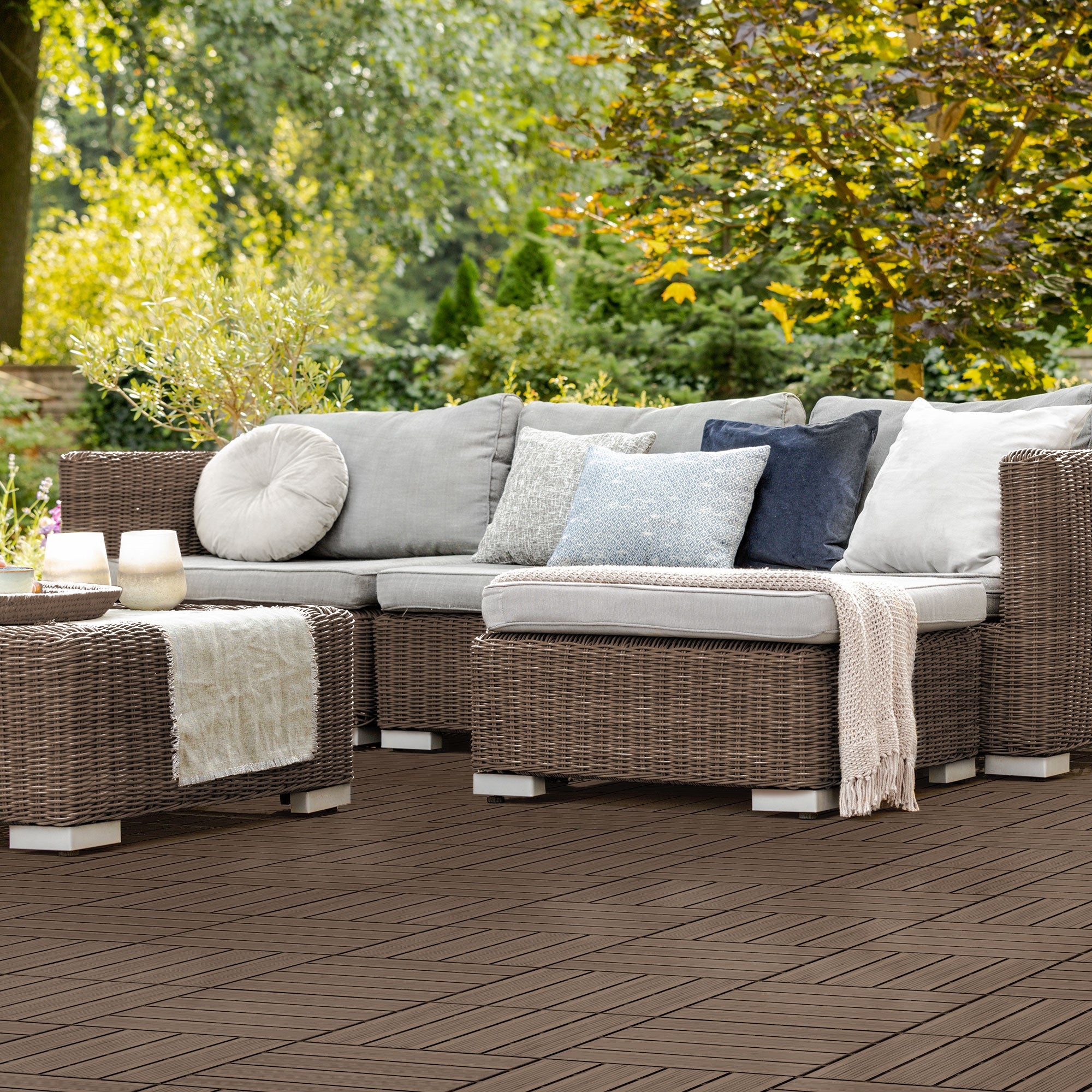 Gemütliche Sitzecke im Garten mit Sofa und Kissen auf einer Holzterrasse.