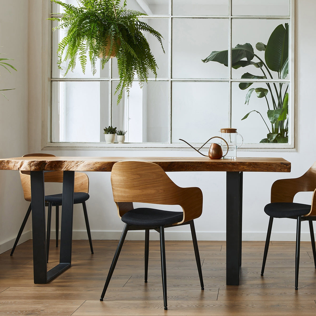 Ein Tisch aus Holz mit vier Stühlen in einem hellen Raum mit Pflanzen im Hintergrund.