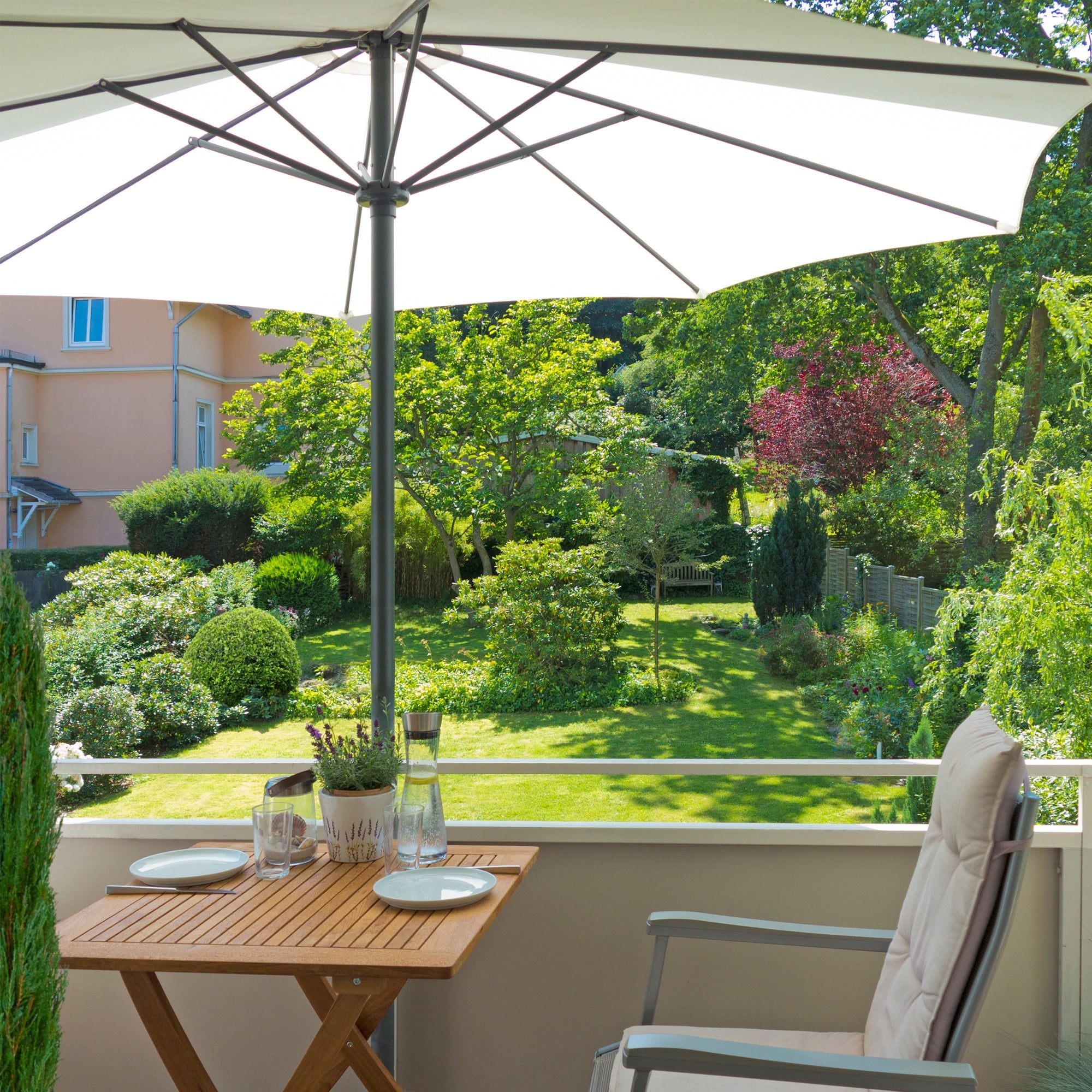 Terrasse mit einem Sonnenschirm, Tisch und Stühlen, umgeben von einem Garten.