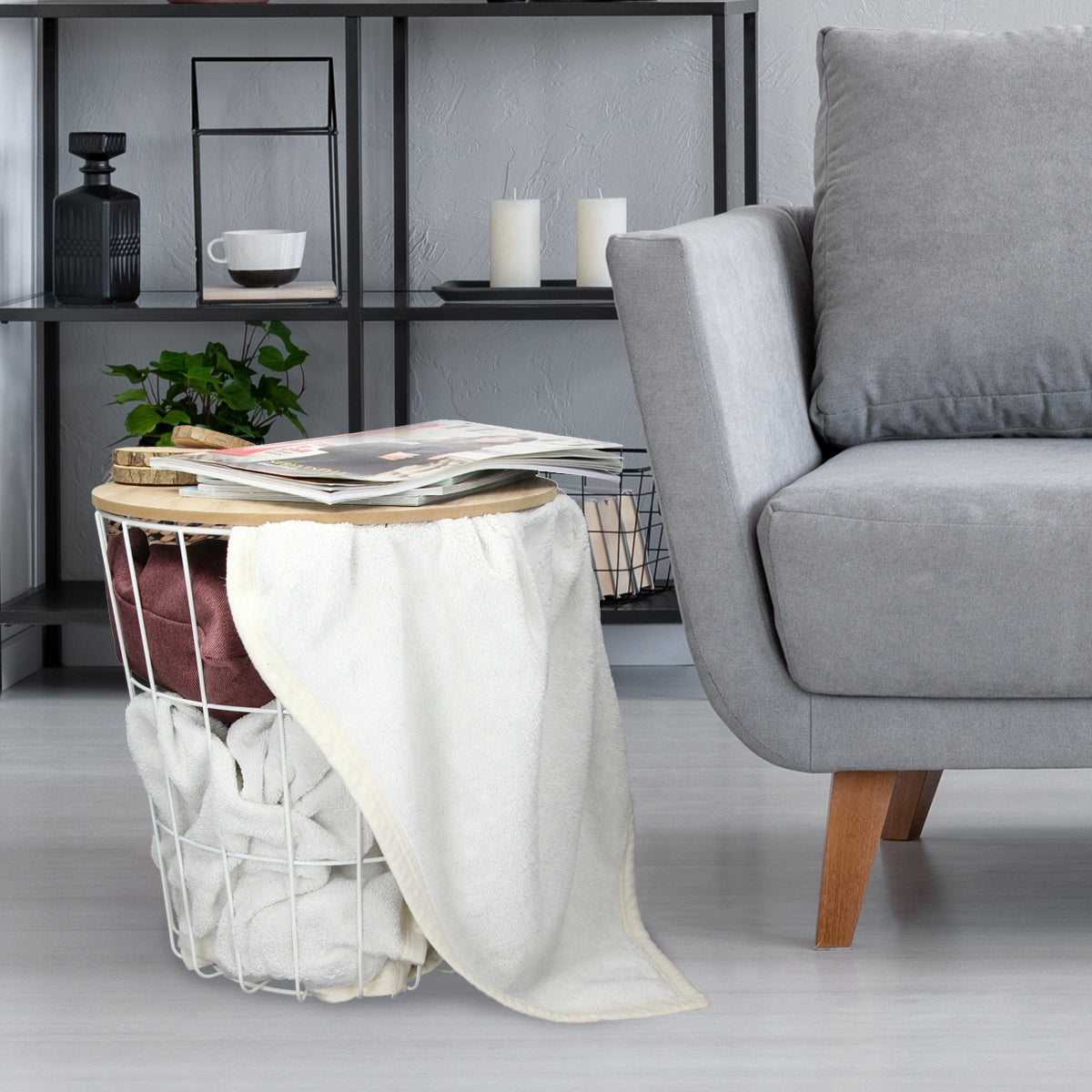 Ein runder Tisch mit einem Korb und einer Decke neben einem grauen Sofa.