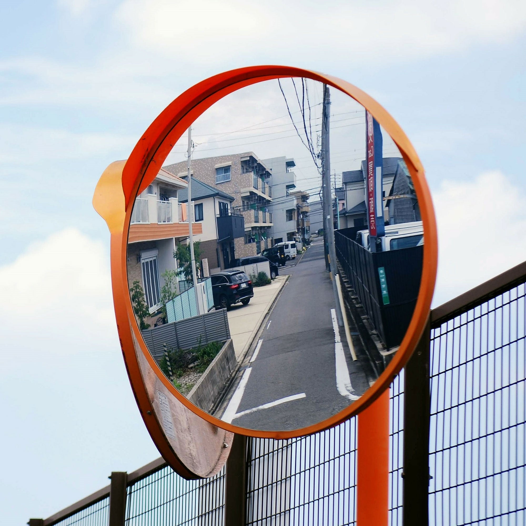 Runder Verkehrsspiegel an einer Straße, reflektiert Häuser und eine Straße.