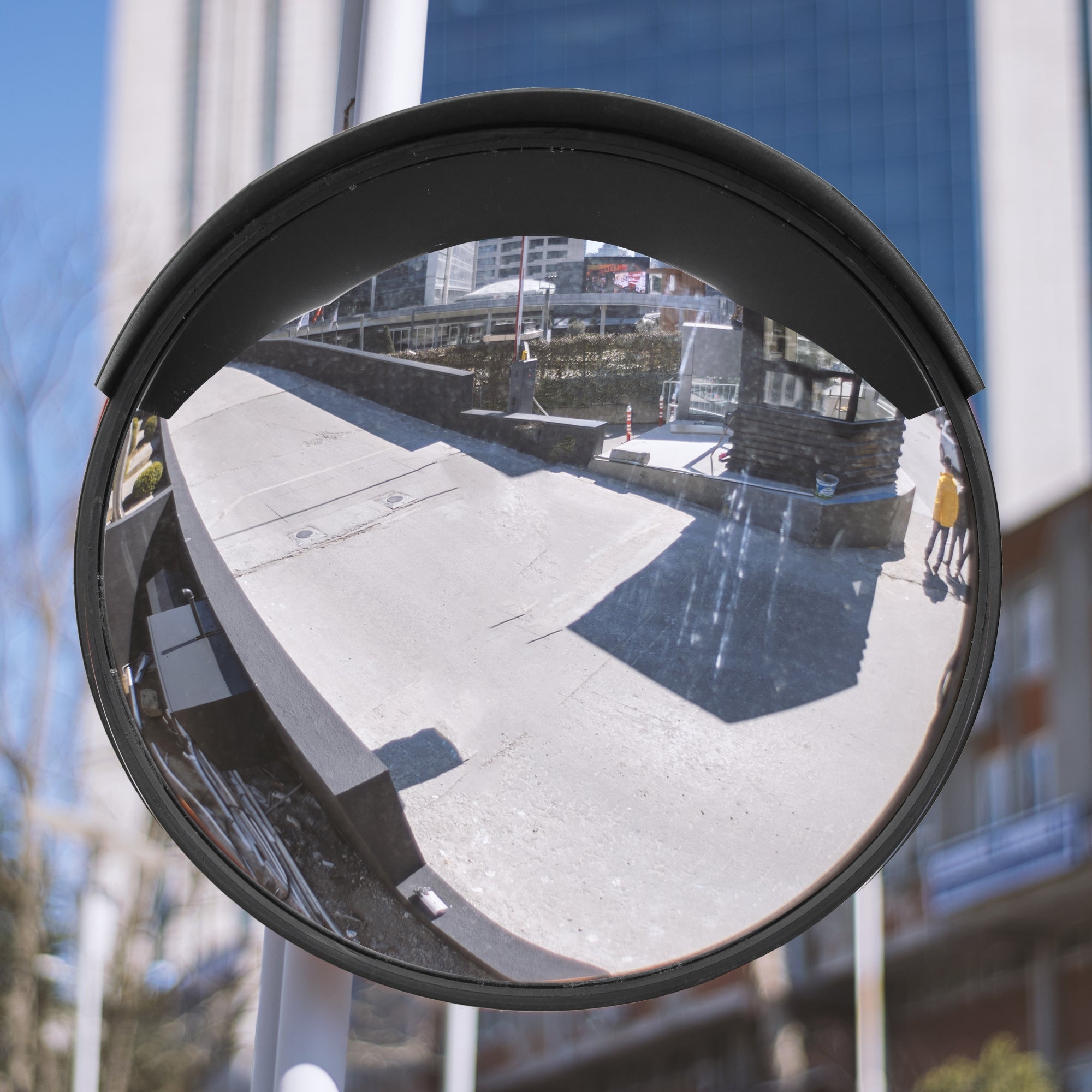 Rund trafik spejl med refleksion af en vej og bygninger i baggrunden.