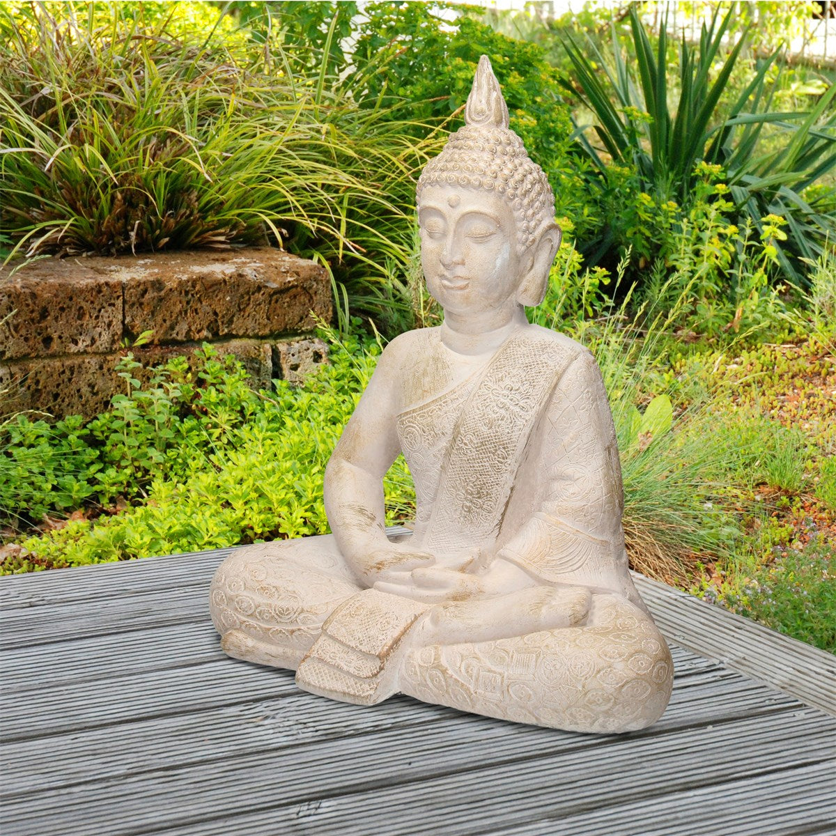 Weiße Buddha-Statue sitzt auf einem Holztisch, umgeben von Pflanzen.