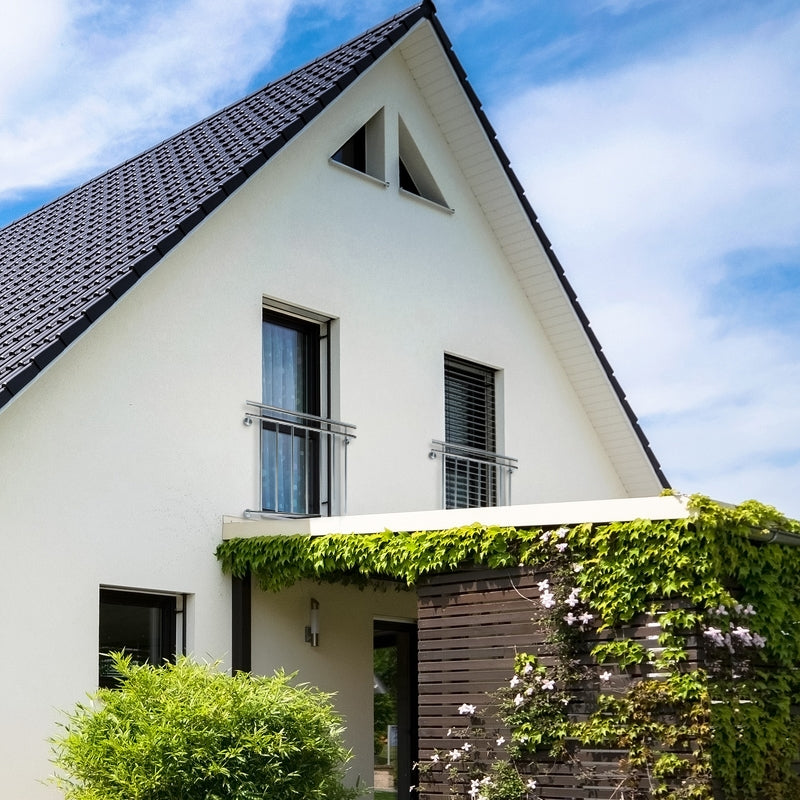 Helles Haus mit Satteldach, begrüntem Eingangsbereich und großen Fenstern.