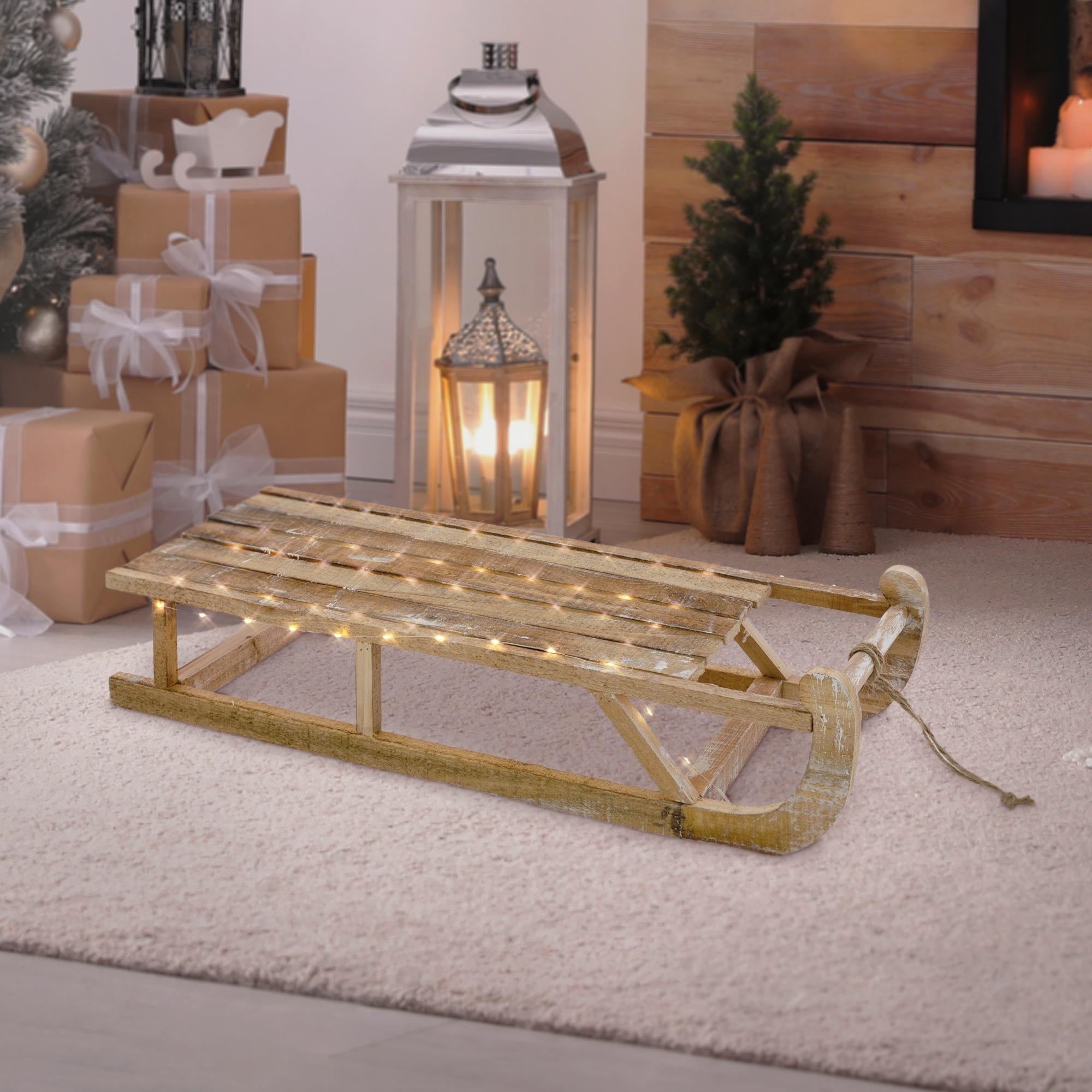 Une luge en bois avec des lumières, à côté d'une lanterne et d'un sapin de Noël.