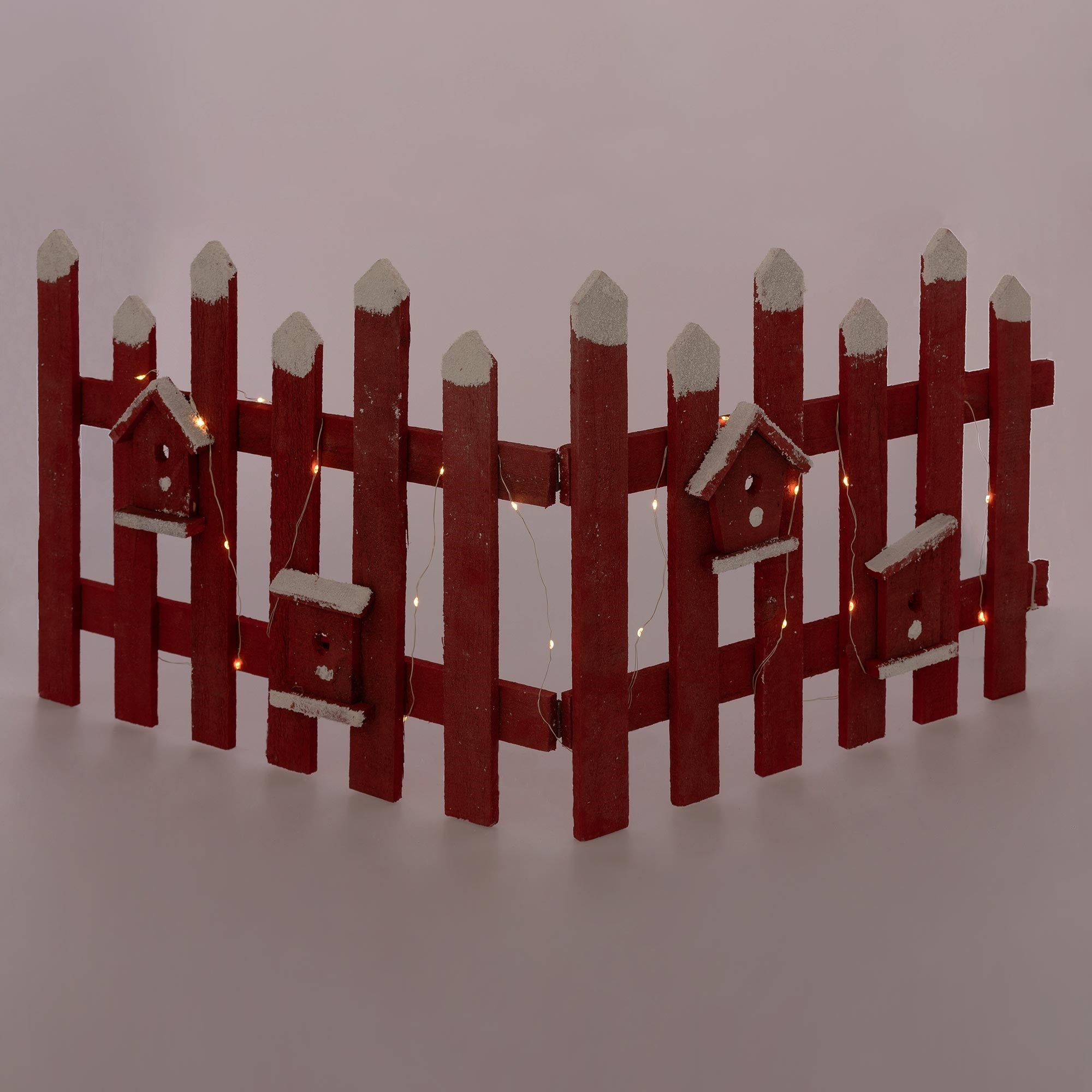 Ein roter Holzzaun mit kleinen Vogelhäusern und Lichtern.