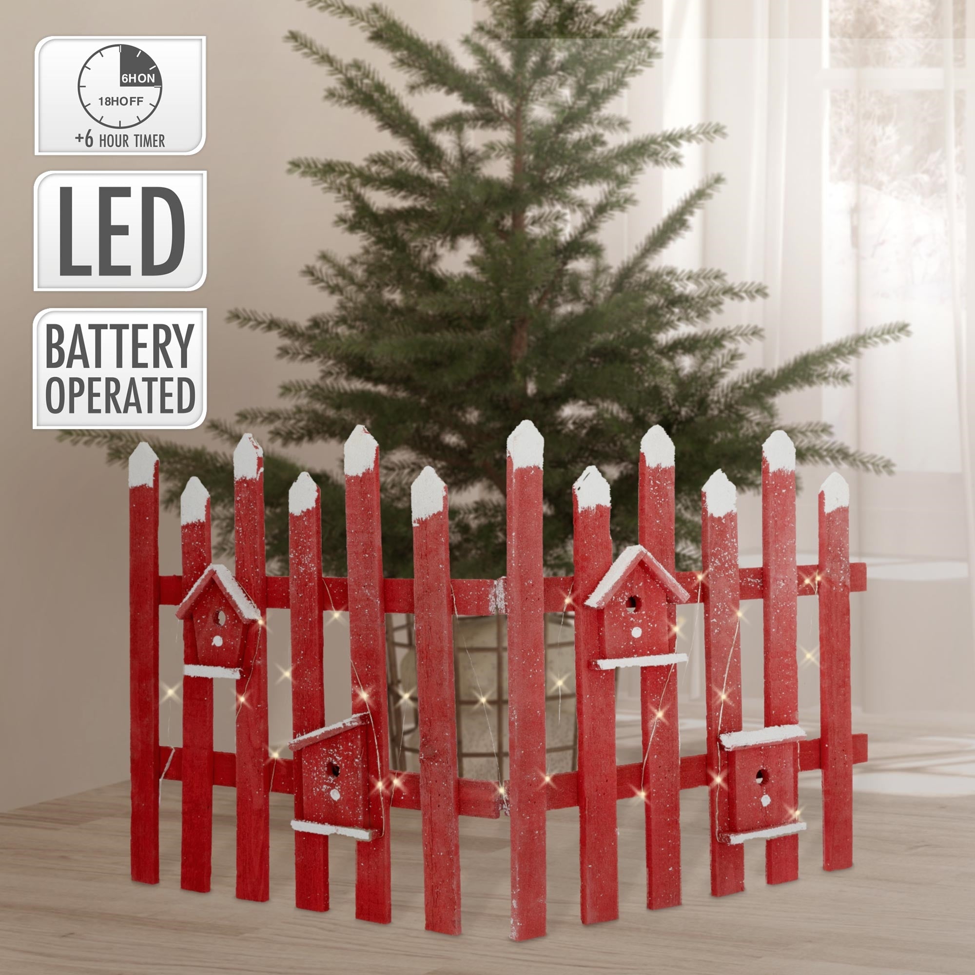 Rote Holzlattenzaun mit Vogelhäuschen, vor einem Weihnachtsbaum im Hintergrund.