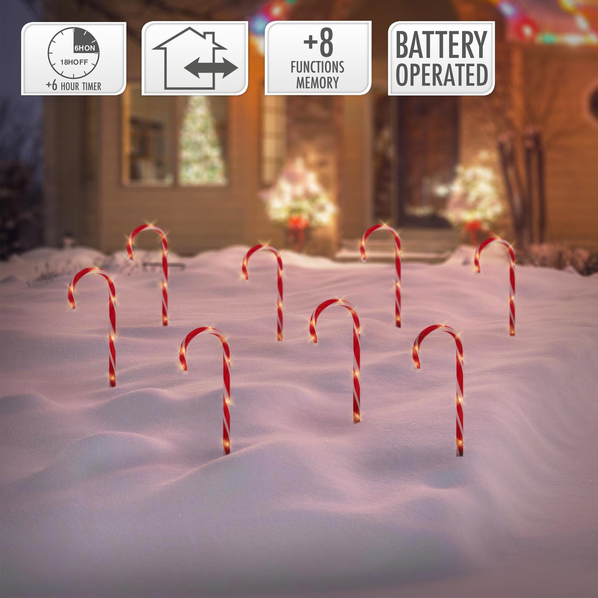 Mehrere rot-weiße Zuckerstangen stehen im Schnee vor einem festlich dekorierten Haus.