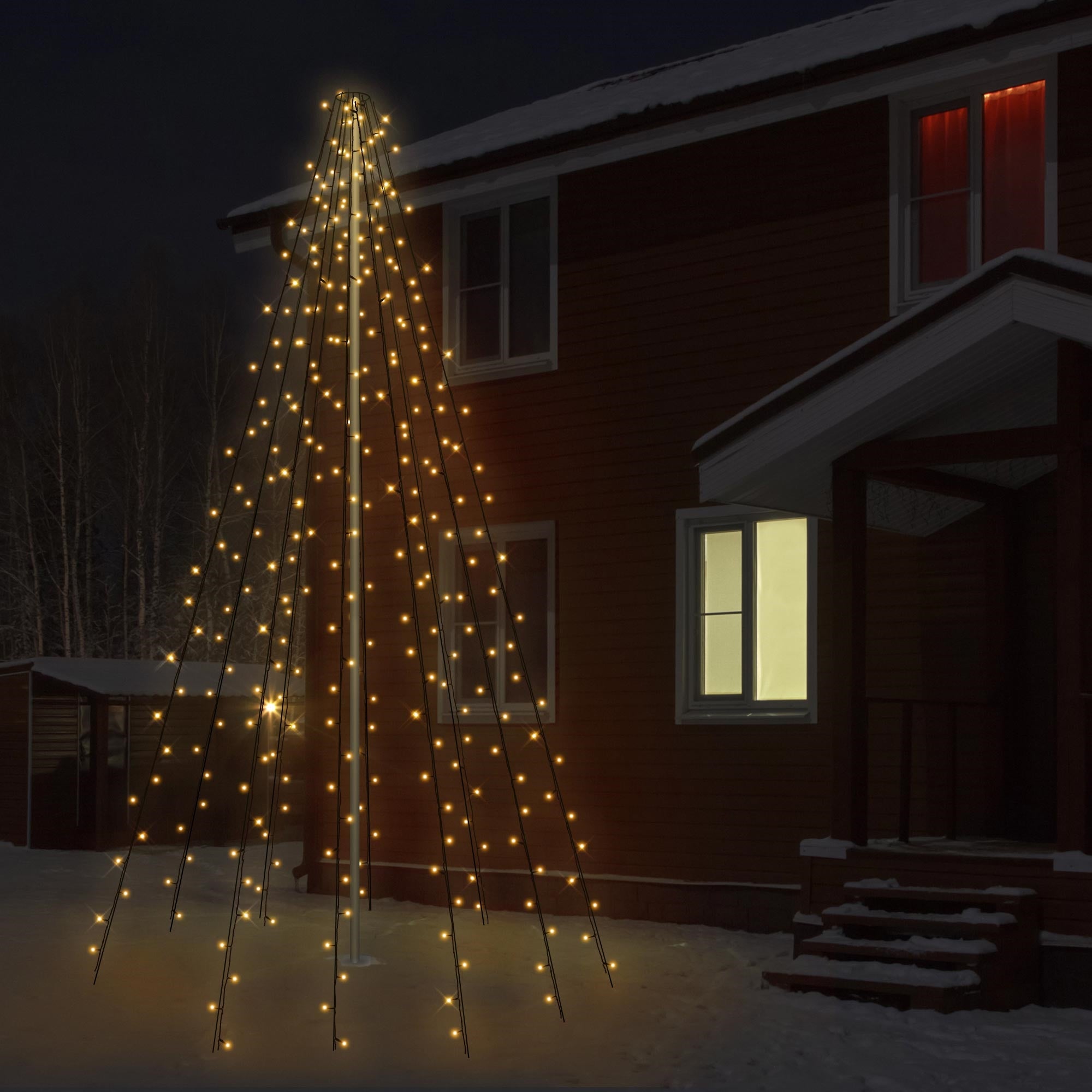 Verlichte kerstboom van lichten voor een houten huis in de sneeuw bij nacht.