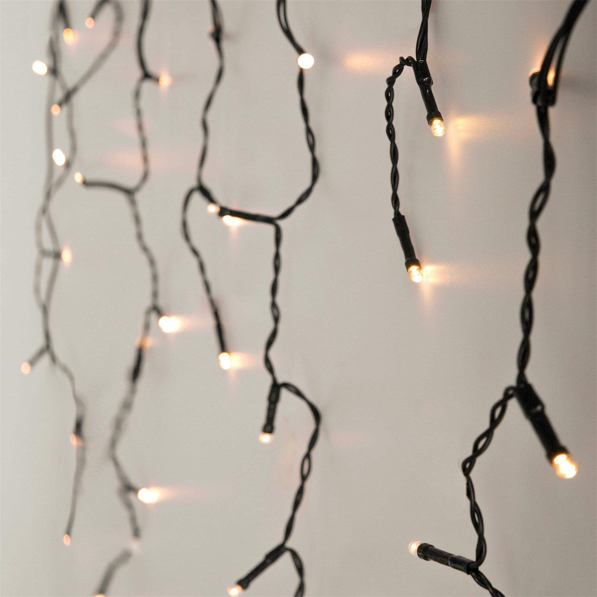Lichterkette mit kleinen, leuchtenden Lampen an einem weißen Hintergrund.