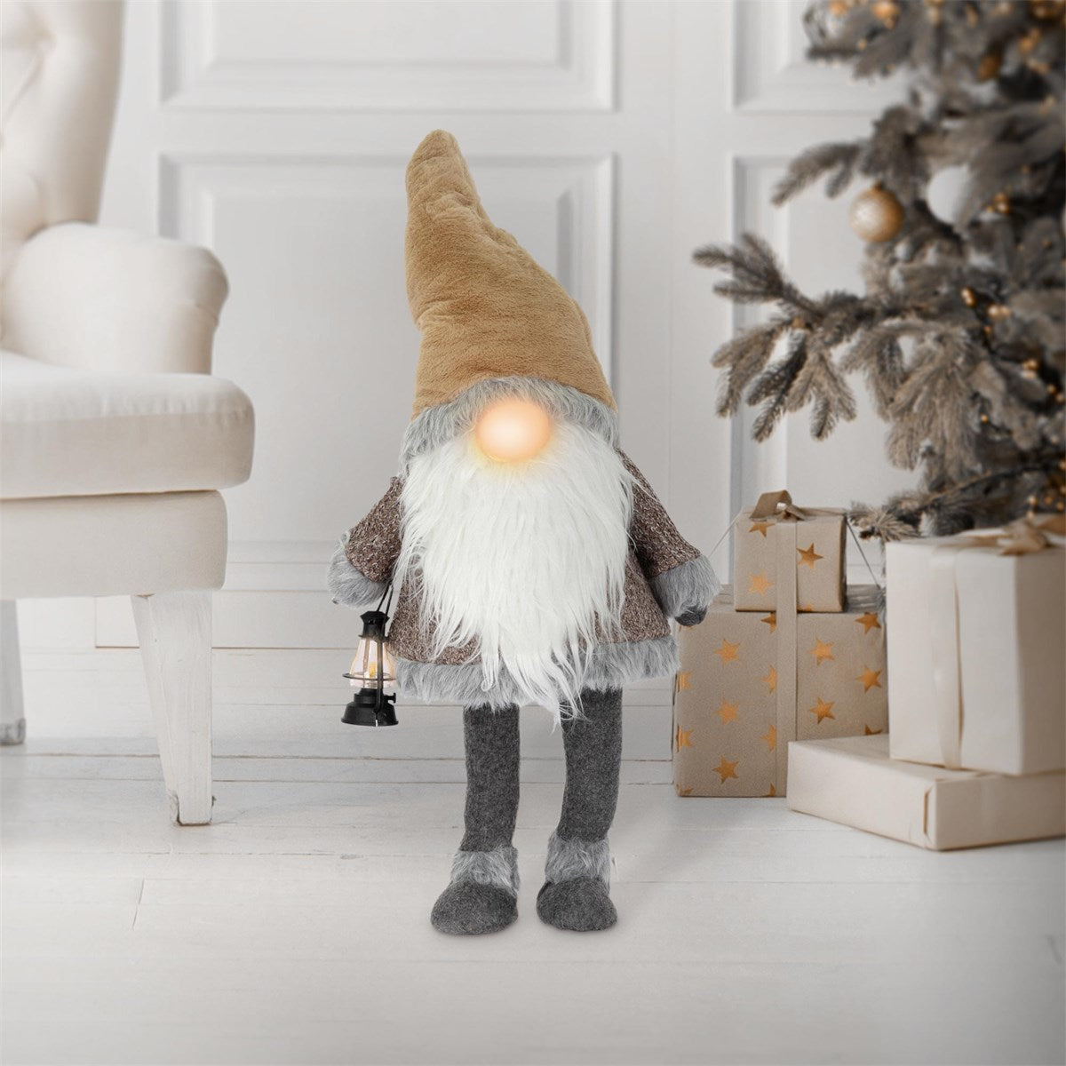 Ein grauer Wichtel mit einer Laterne steht neben einem Weihnachtsbaum.