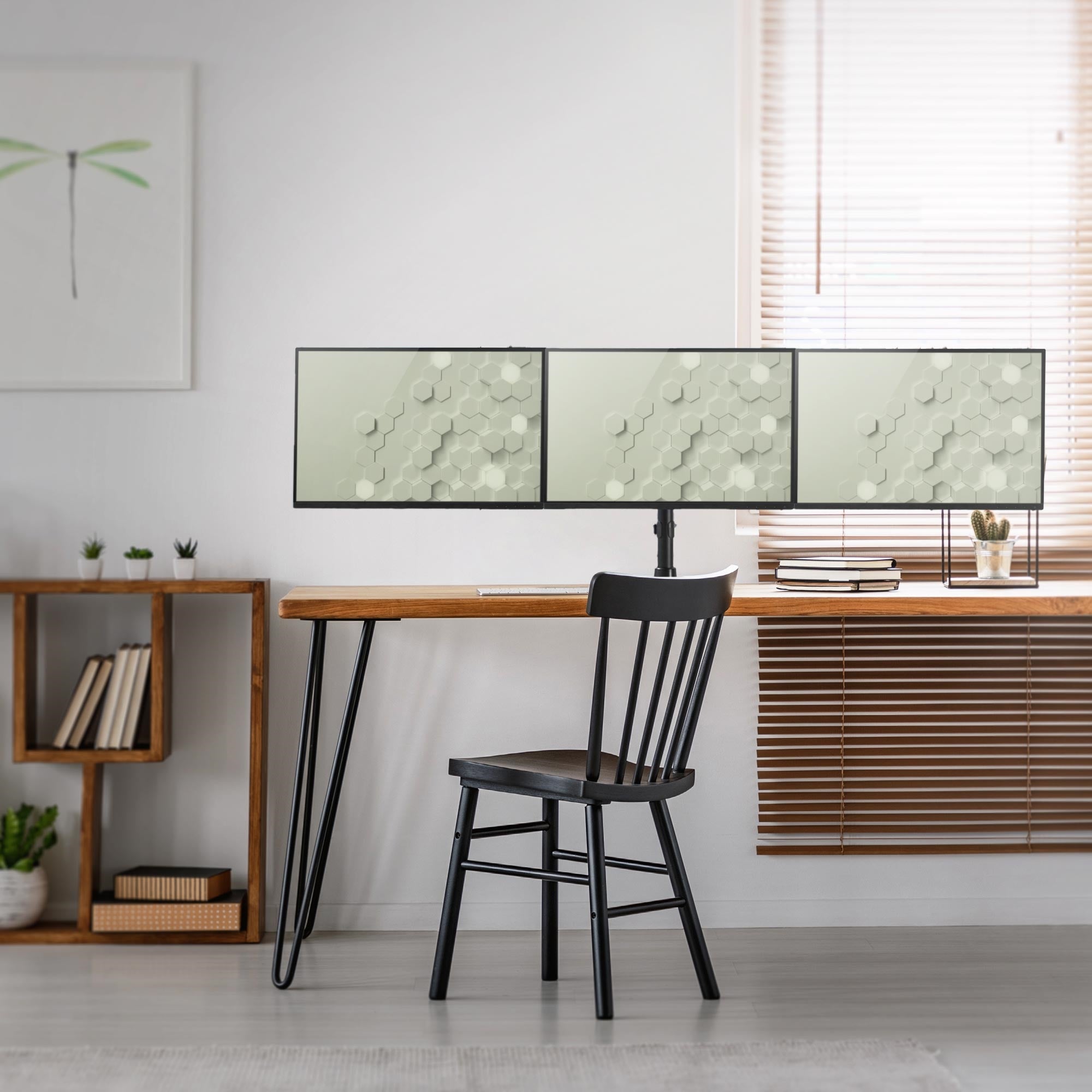 Schreibtisch mit drei Monitoren, schwarzem Stuhl und Pflanzen im Hintergrund.