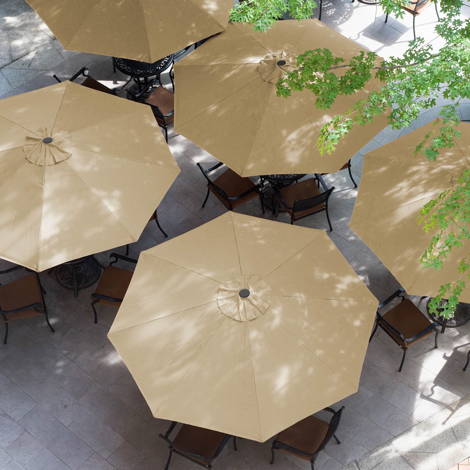 Mehrere beige Sonnenschirme über Tischen in einem Innenhof mit Bäumen.