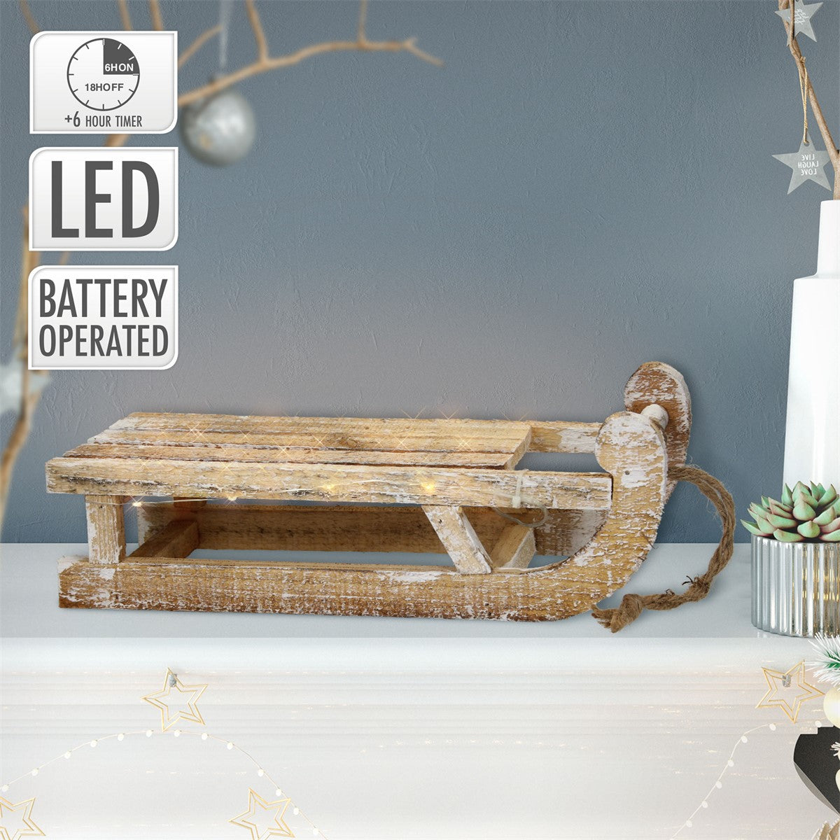 Holzschlitten mit LED-Beleuchtung, auf einem Tisch vor grauer Wand.