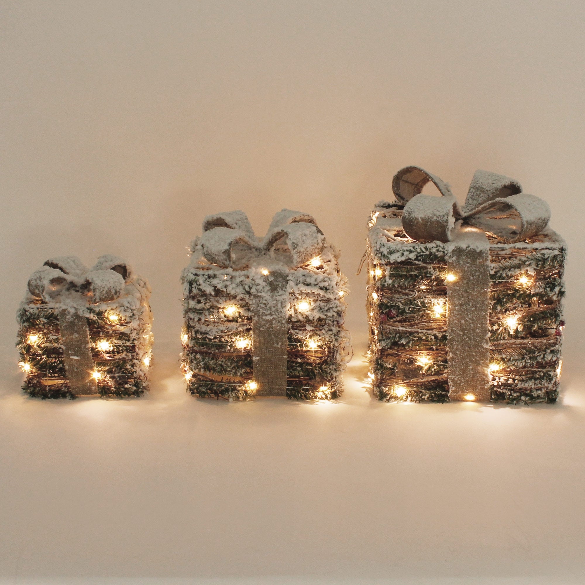 Drei Geschenke mit Schleifen und Lichtern, in verschiedenen Größen, auf hellem Hintergrund.