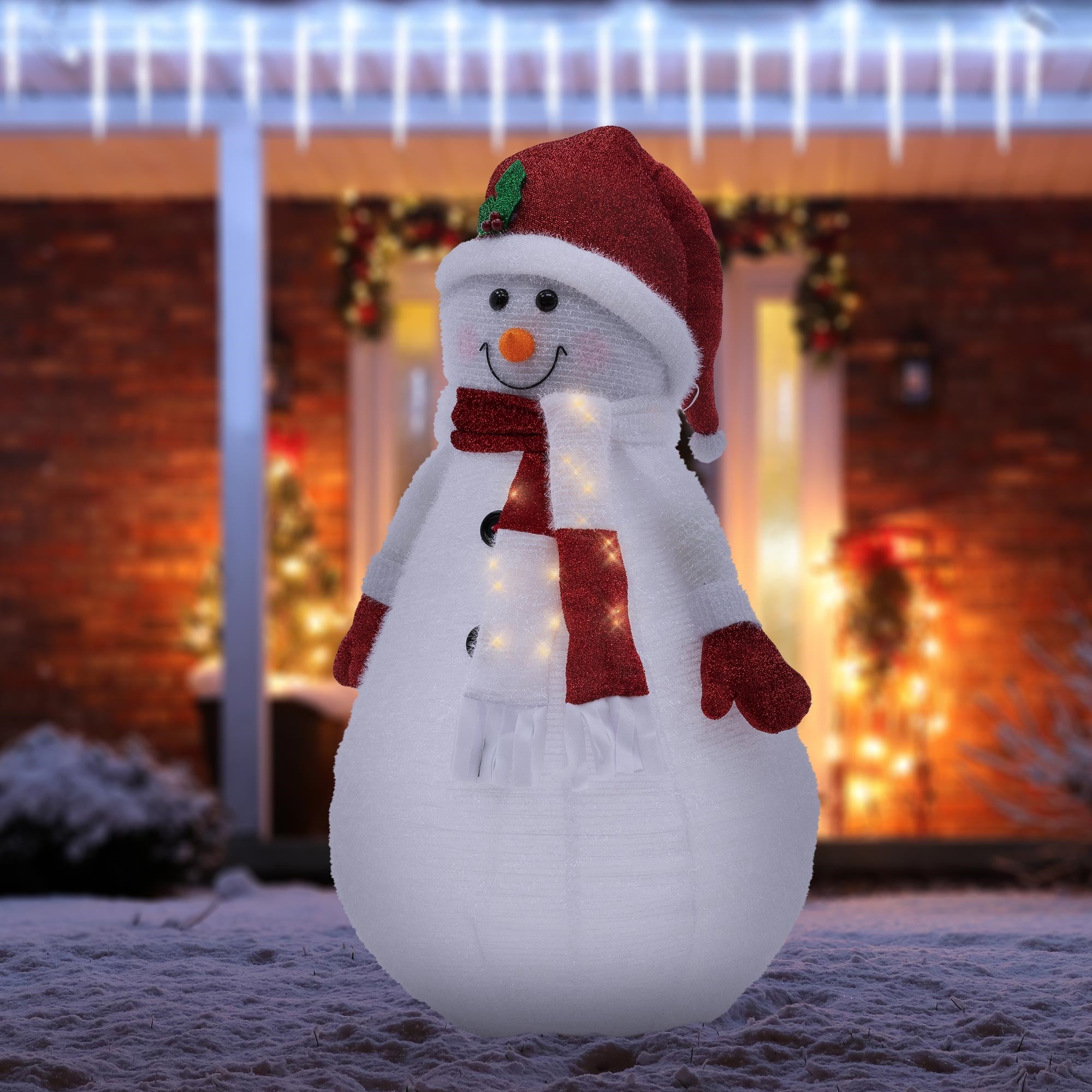 Beleuchteter Schneemann mit rotem Hut und Schal im Schnee.