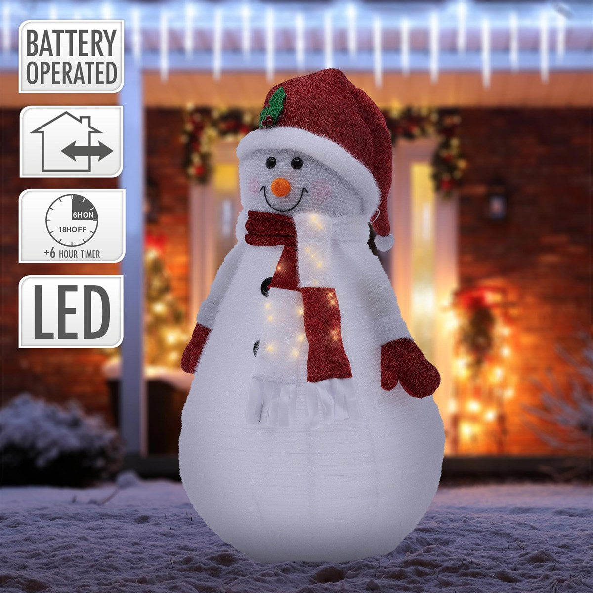 Plyšová figurka sněhuláka s vánoční čepicí a LED světly před slavnostně vyzdobeným domem.