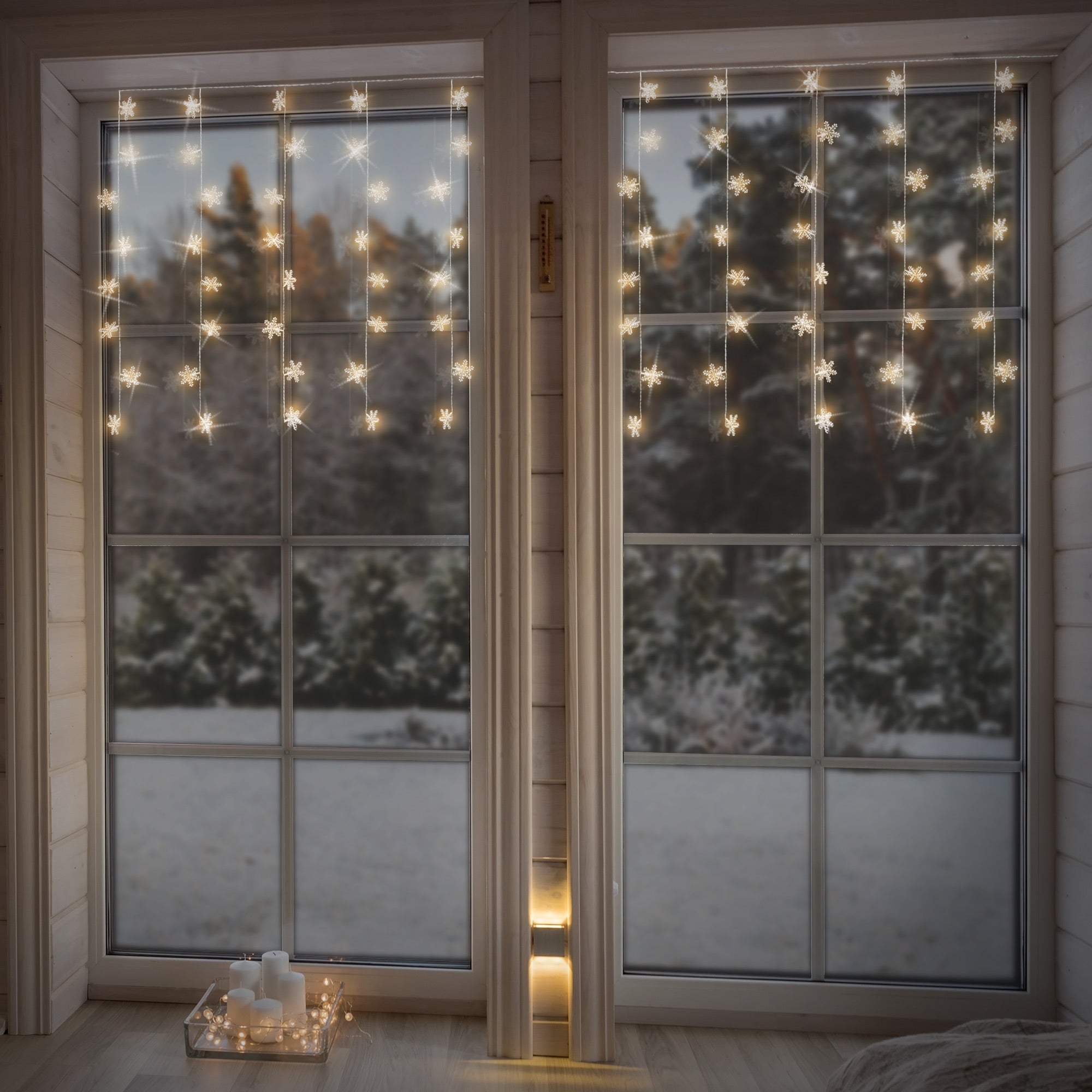 Finestra con catena luminosa e fiocchi di neve, paesaggio invernale sullo sfondo.
