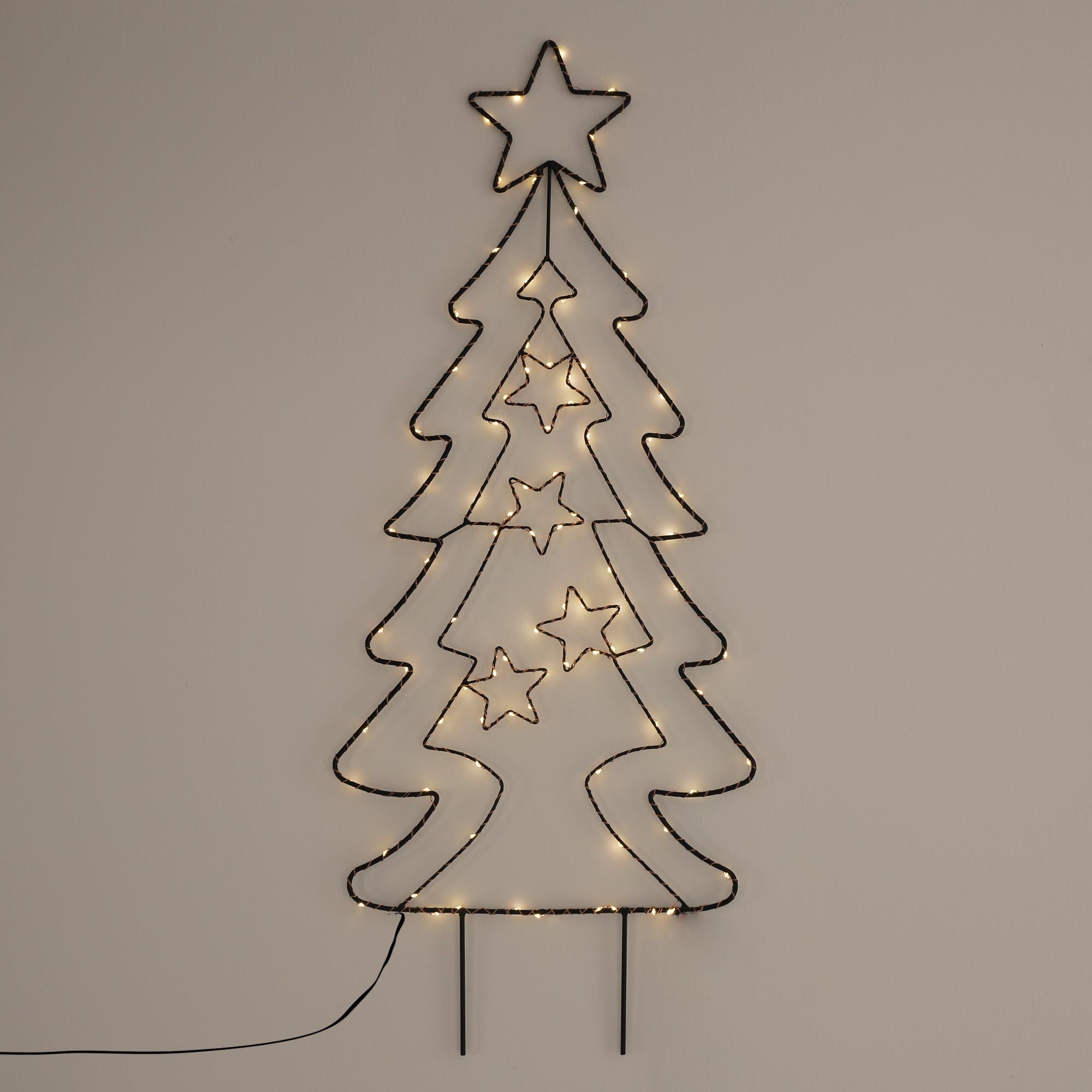 Trådt træ med lys, formet som et juletræ, på en væg.