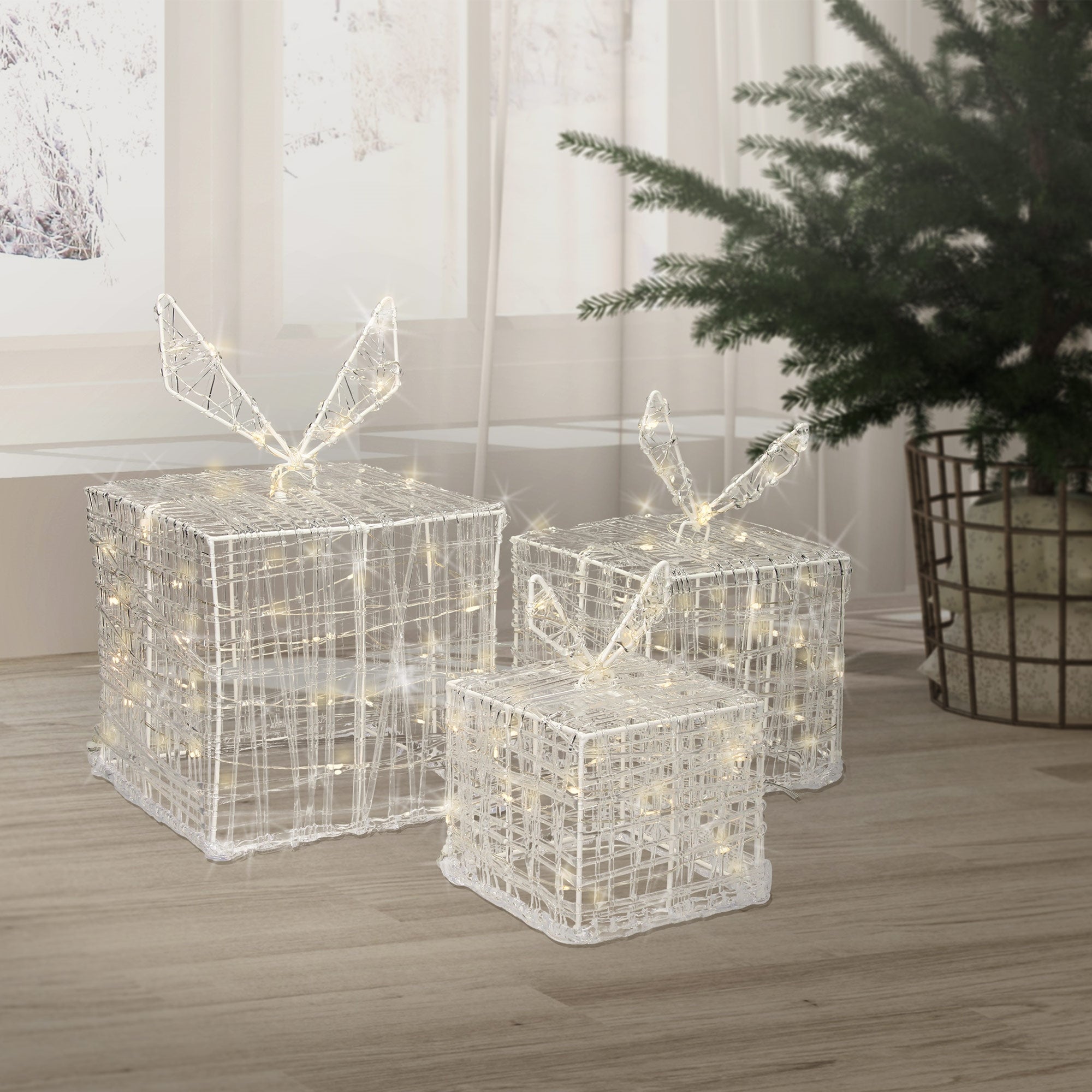 Three gift boxes made of wire with bows, standing in front of a Christmas tree.