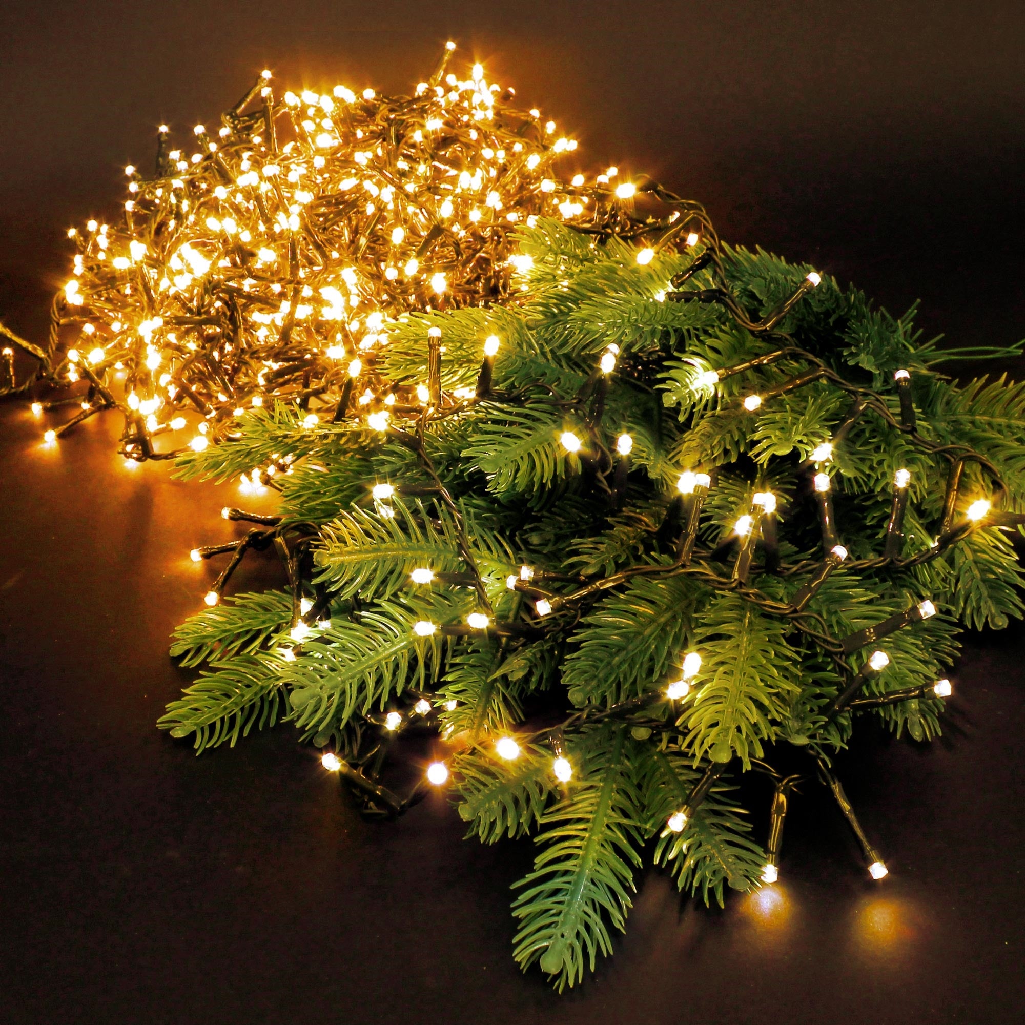Lichterkette auf Tannenzweigen, auf schwarzem Hintergrund.