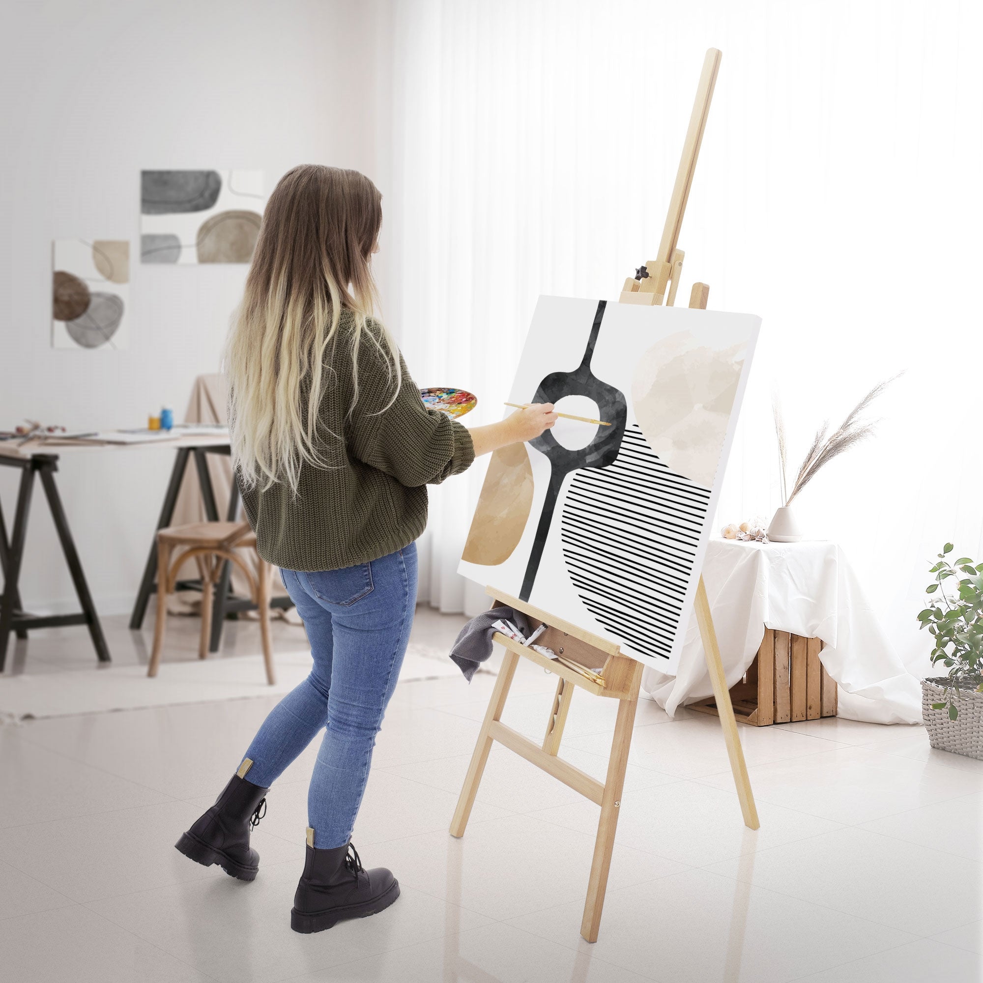 Woman standing in front of an easel and painting with a brush on a canvas.