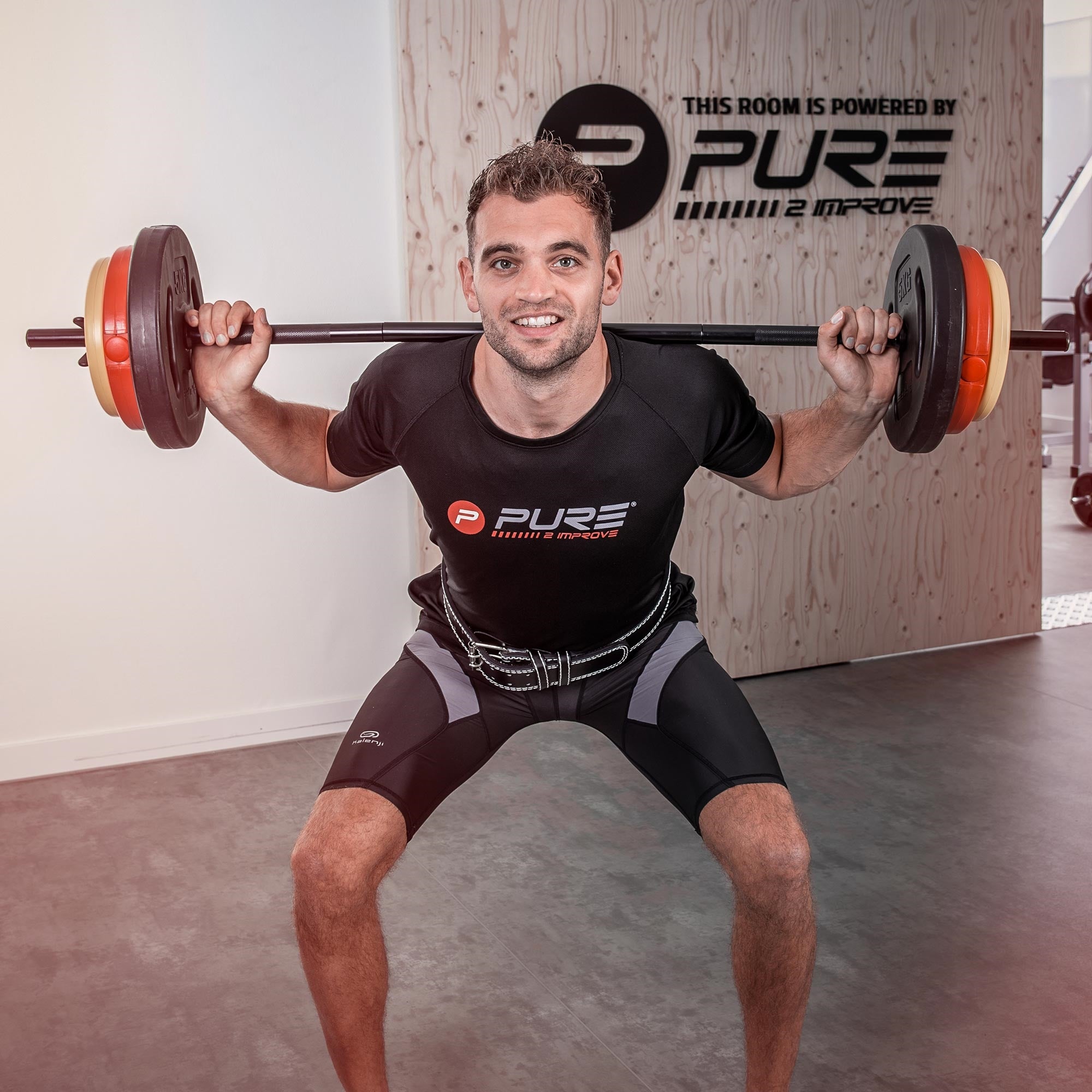 Lächelnder Mann mit Gewicht beim Kniebeugen im Fitnessstudio.