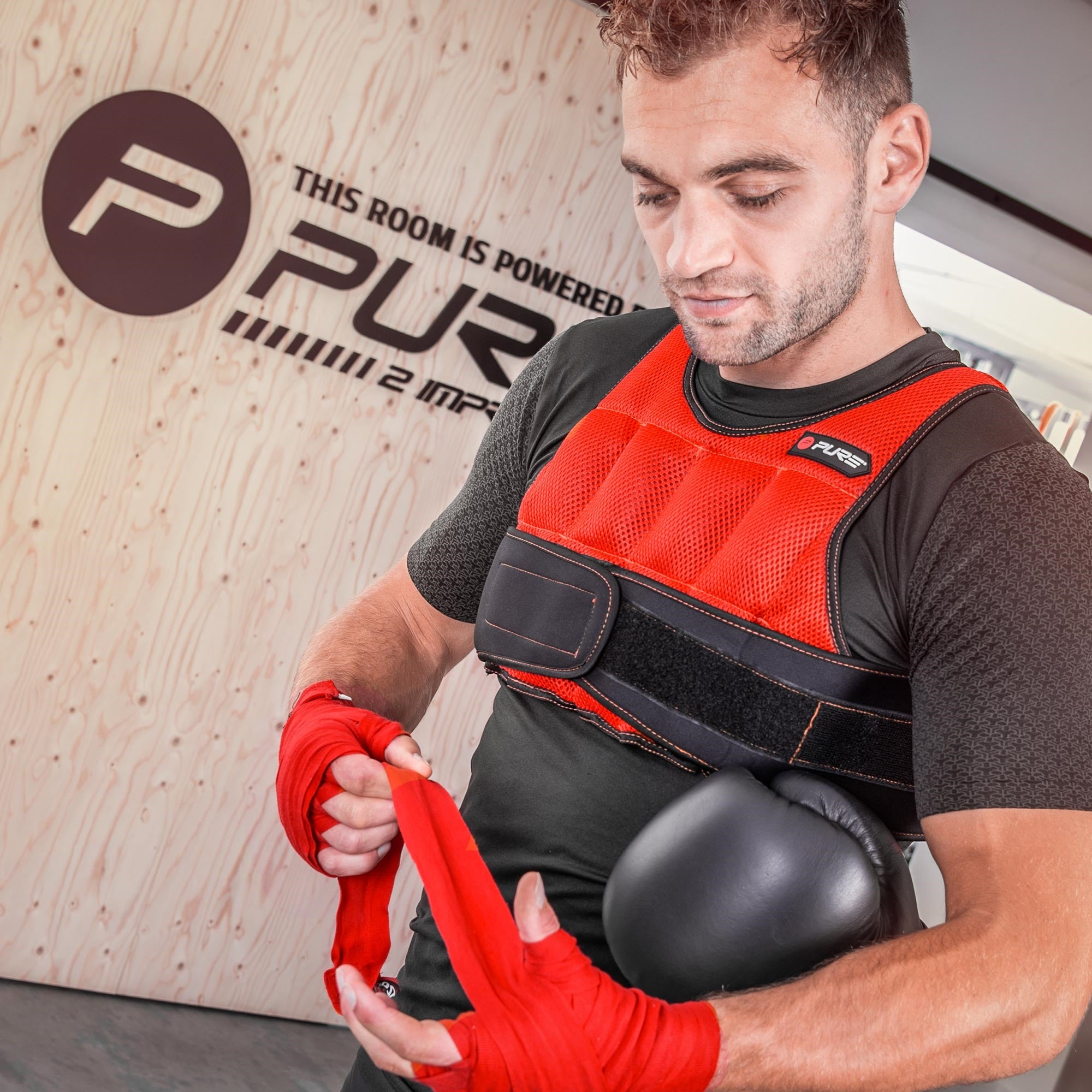 Ein Mann trägt eine rote Trainingsweste und zieht seine Boxhandschuhe an.