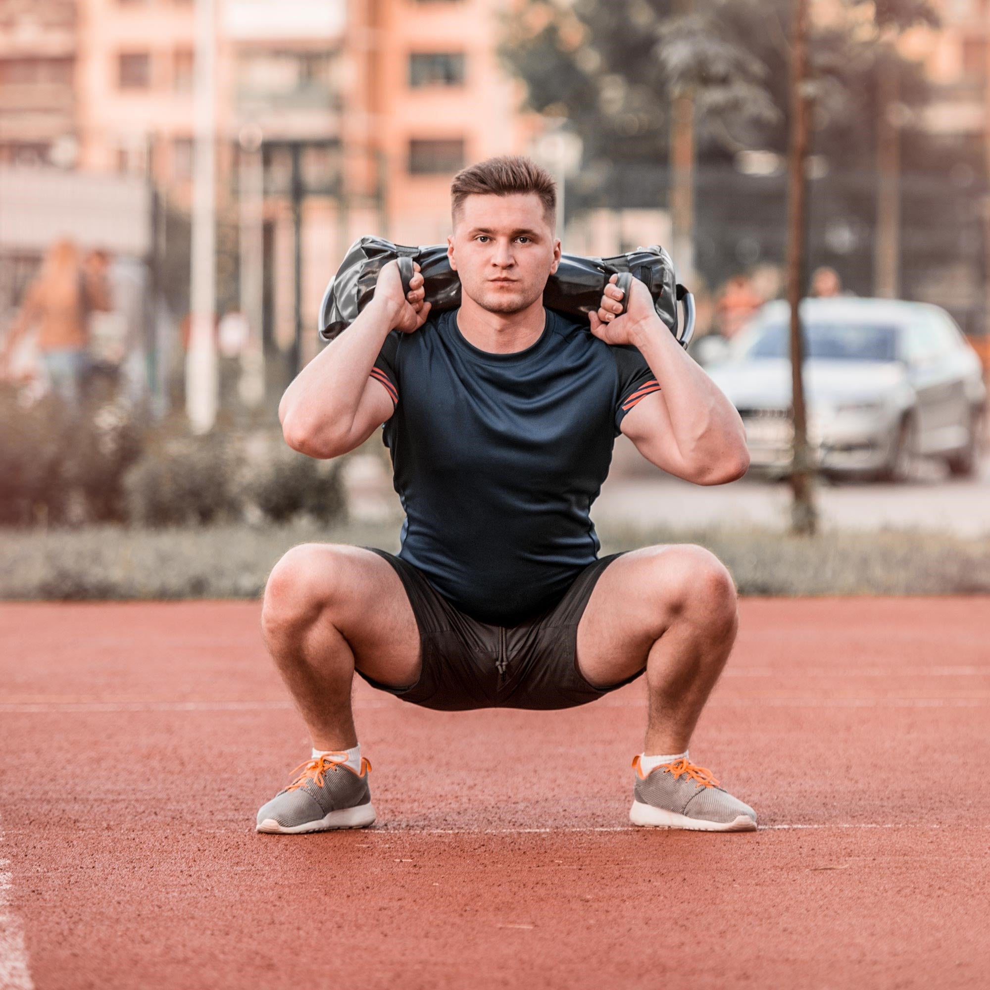 Hombre en ropa deportiva haciendo sentadillas con un Powerbag en la espalda.