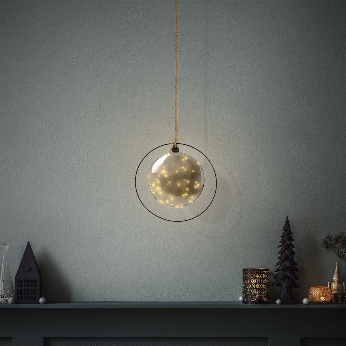 Hängende Glaskugel mit Lichtern vor einer grauen Wand.