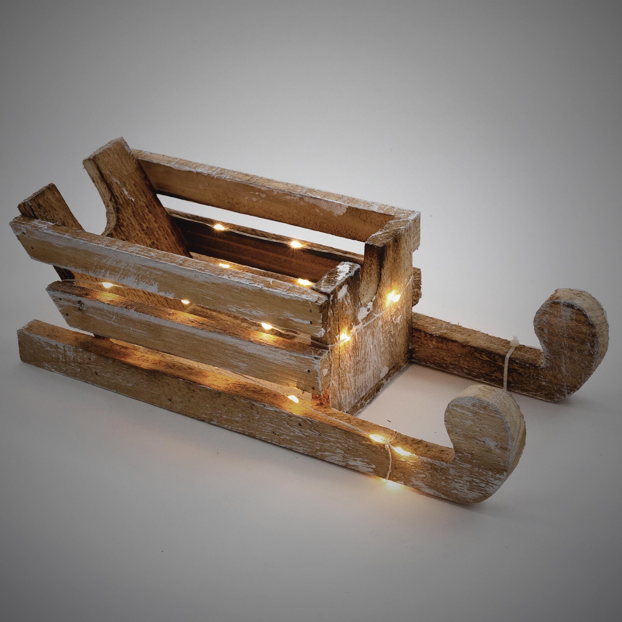 Trineo de madera con luces, sobre fondo gris, en estilo rústico.