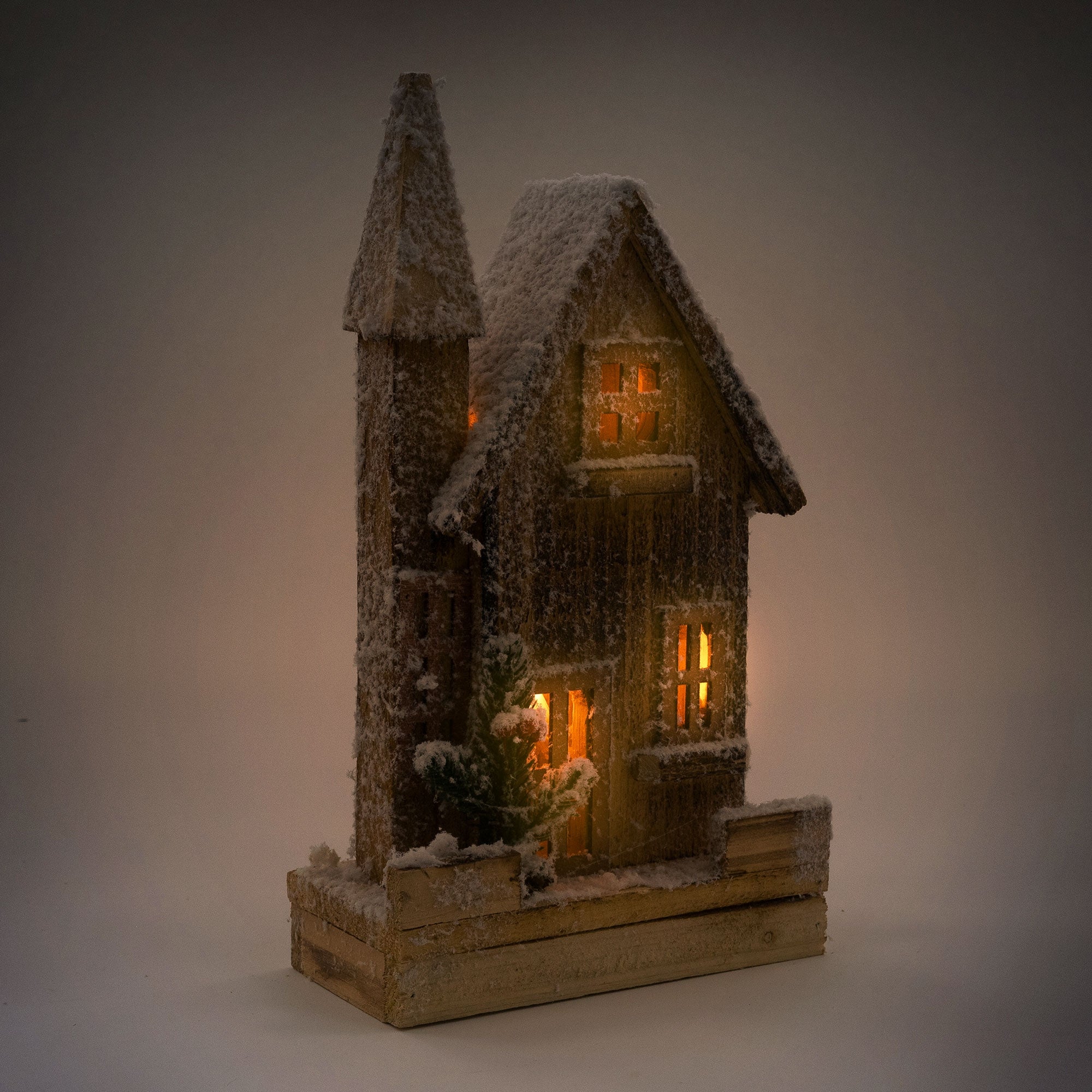 Maison en bois illuminée avec de la neige, une lumière chaude et un sapin.