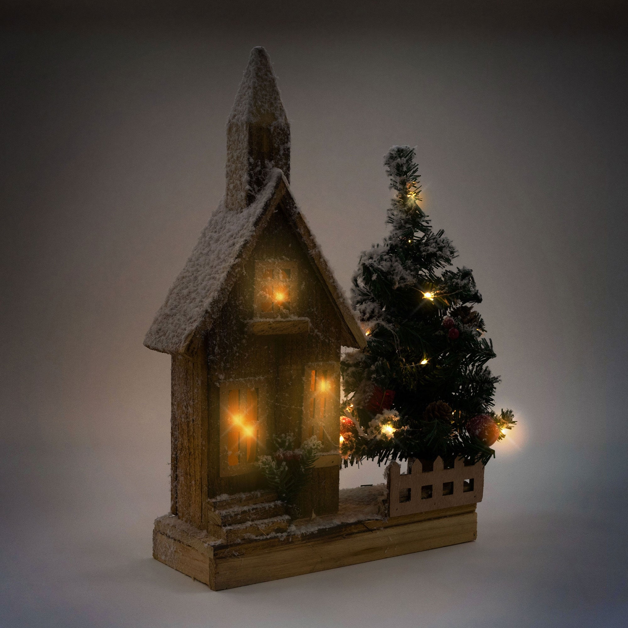 Holzhaus mit Schnee und Lichtern, daneben ein Weihnachtsbaum.