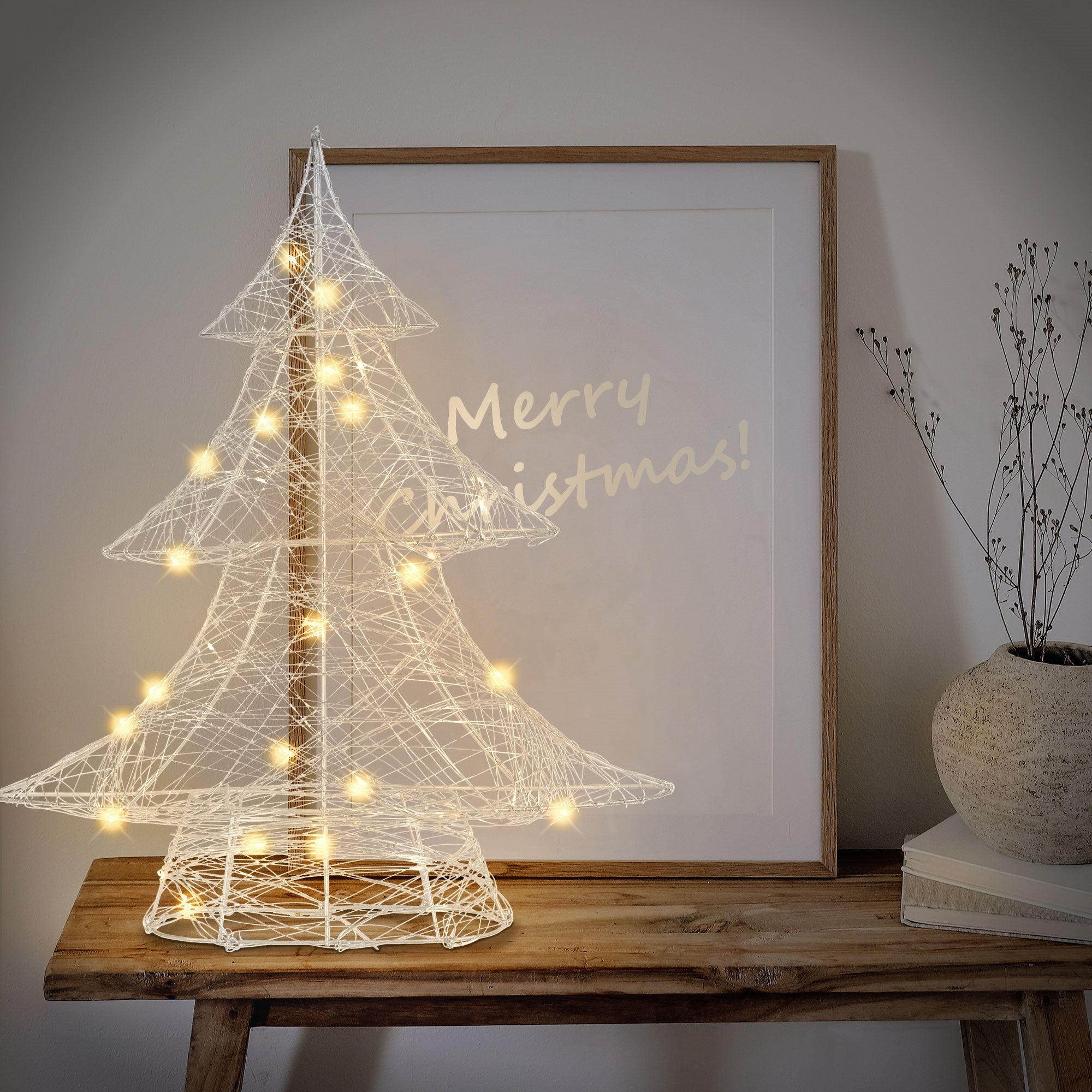 White wire tree with lights in front of a framed picture.