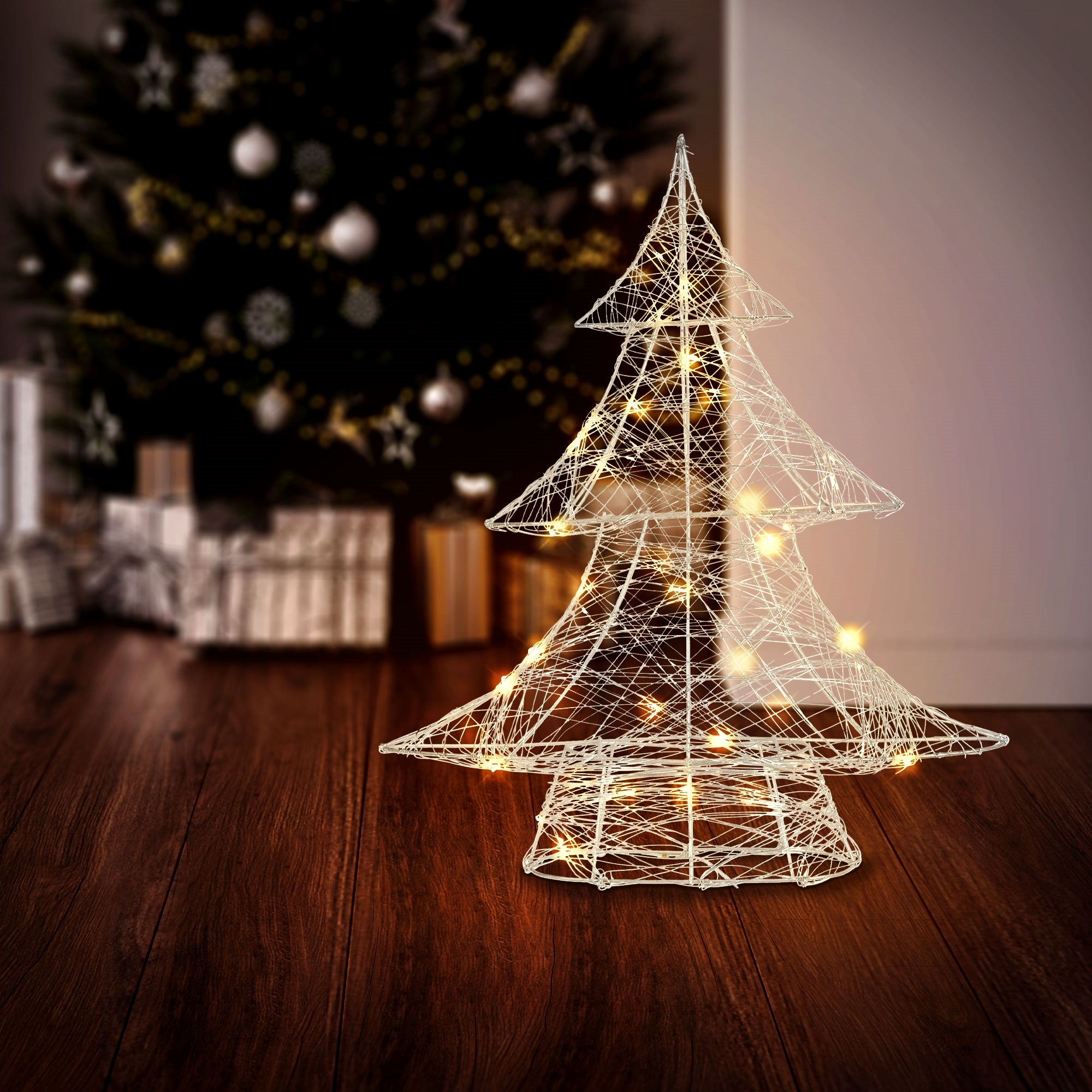 Wire tree with lights in front of a Christmas tree and gifts.
