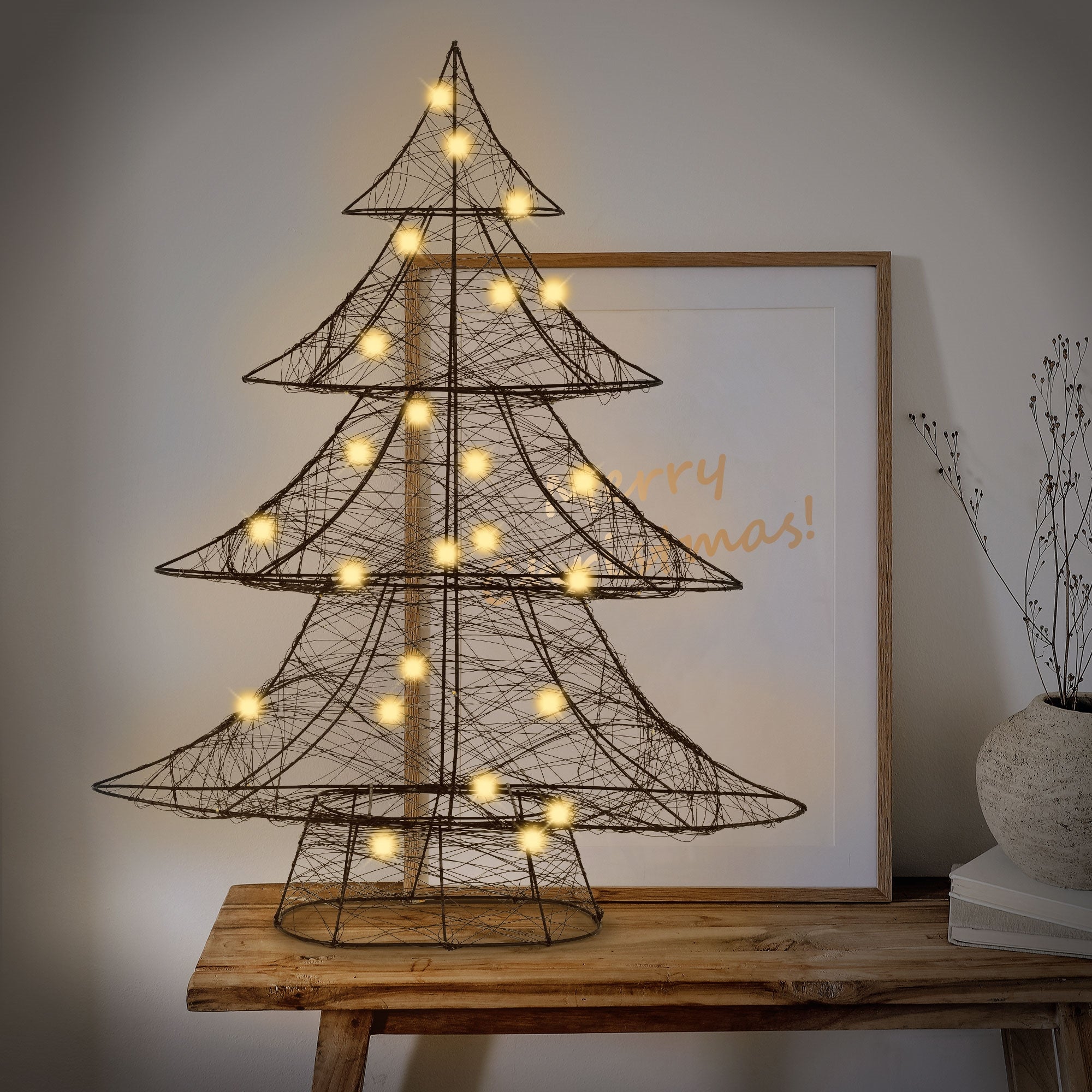 Ein dekorativer Weihnachtsbaum mit Lichtern, neben einem Bild und einer Vase.